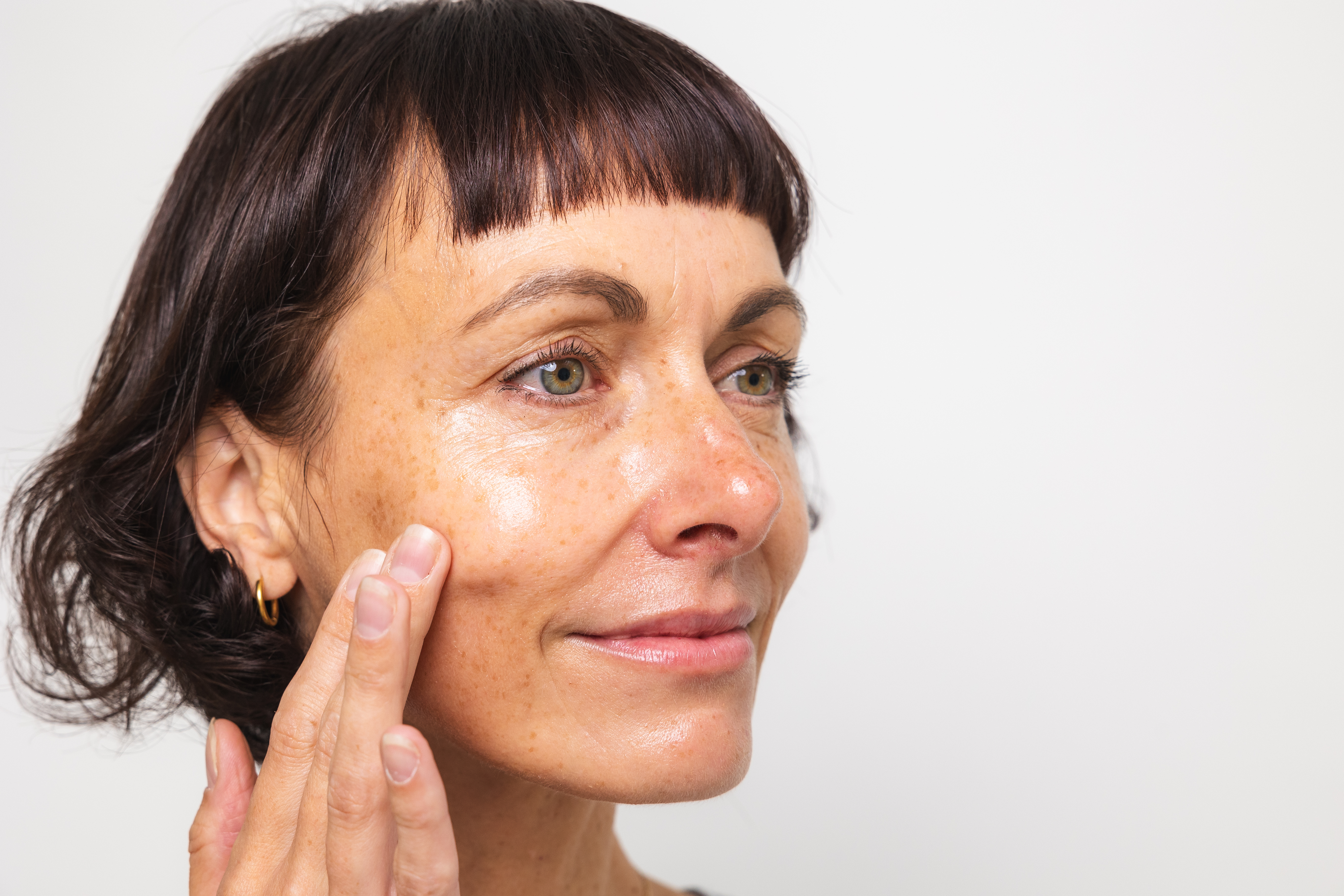 Nahaufnahme einer Frau im Halbprofil, die den Retinal Booster von Beyer & Söhne sanft über ihre Wange streicht und mit einem sanften Lächeln und einem entspannten Gesichtsausdruck an der Kamera vorbeischaut