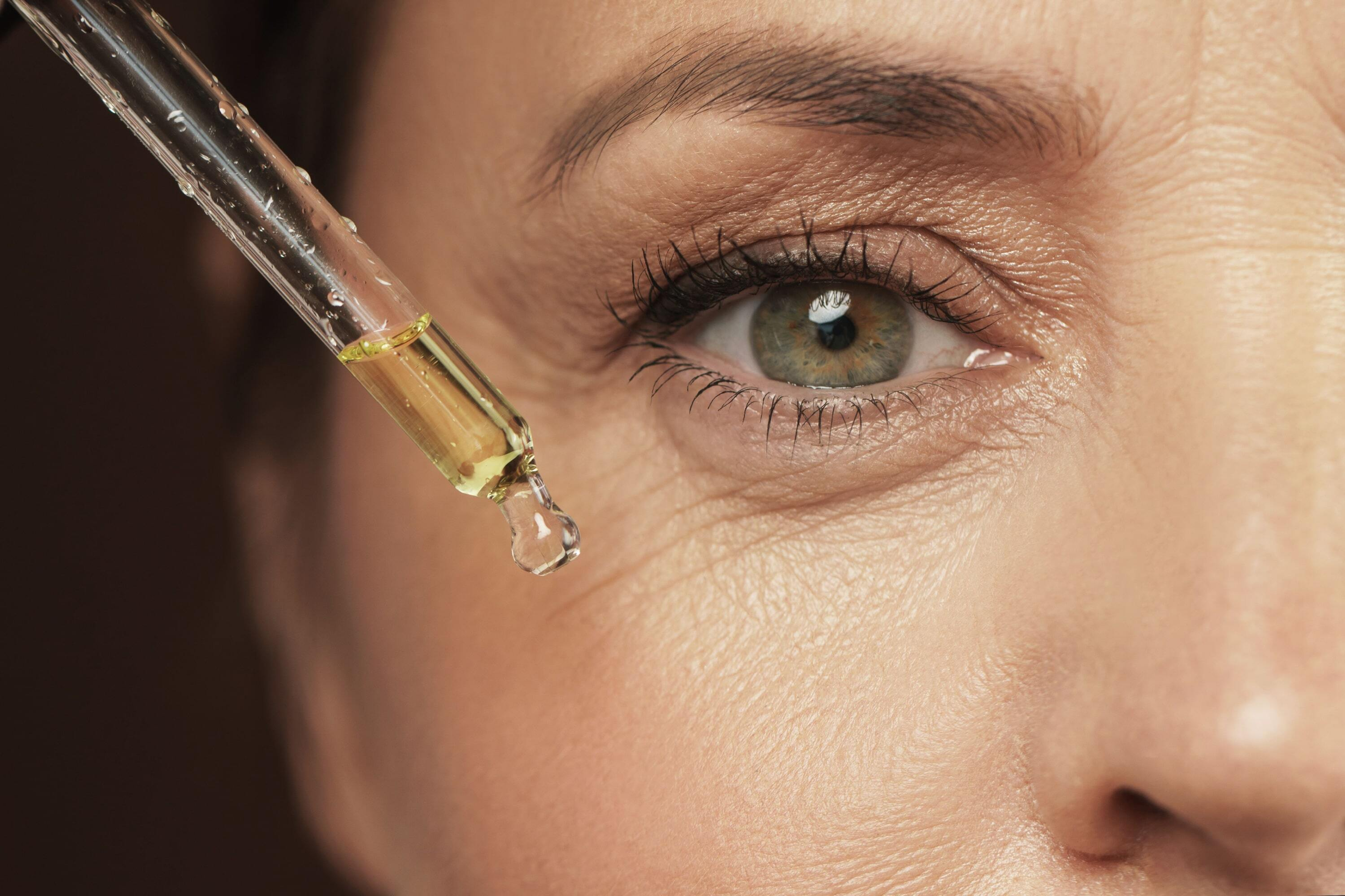 Nahaufnahme einer Frau mit feinen Fältchen um die Augen herum. Die Pipette an der Augenpartie zeigt das Auftragen eines Antioxidantien-Serums.
