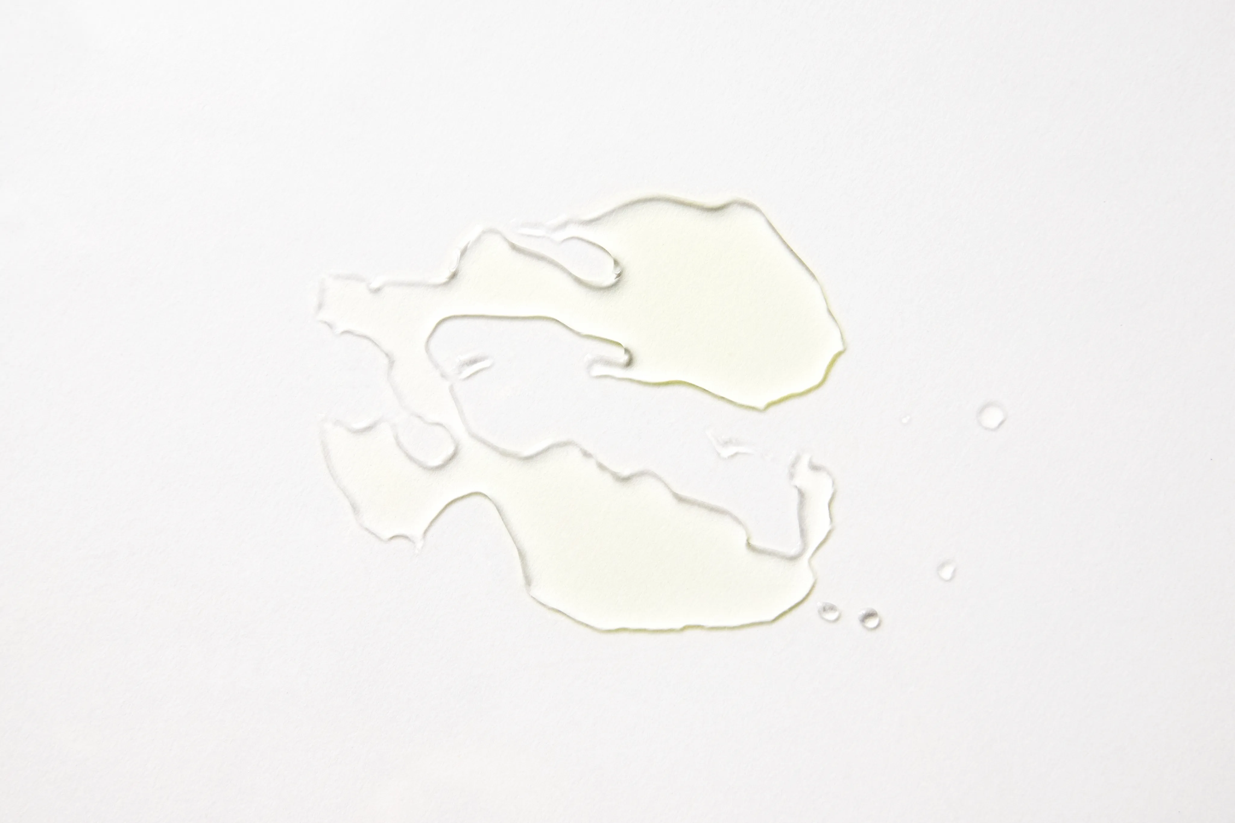 Klecks eines transparenten, hellgelben Fluids auf grauem Hintergrund