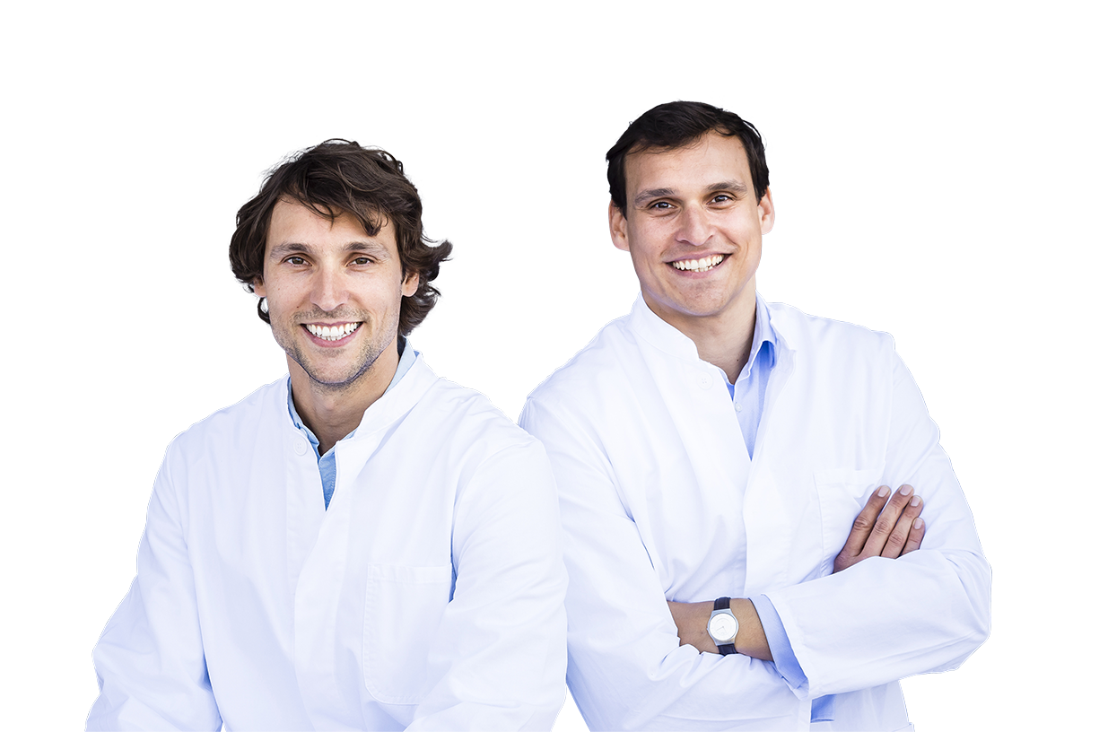 Zwei junge Männer in Arztkitteln schauen mit einem breiten Lächeln sympathisch in die Kamera