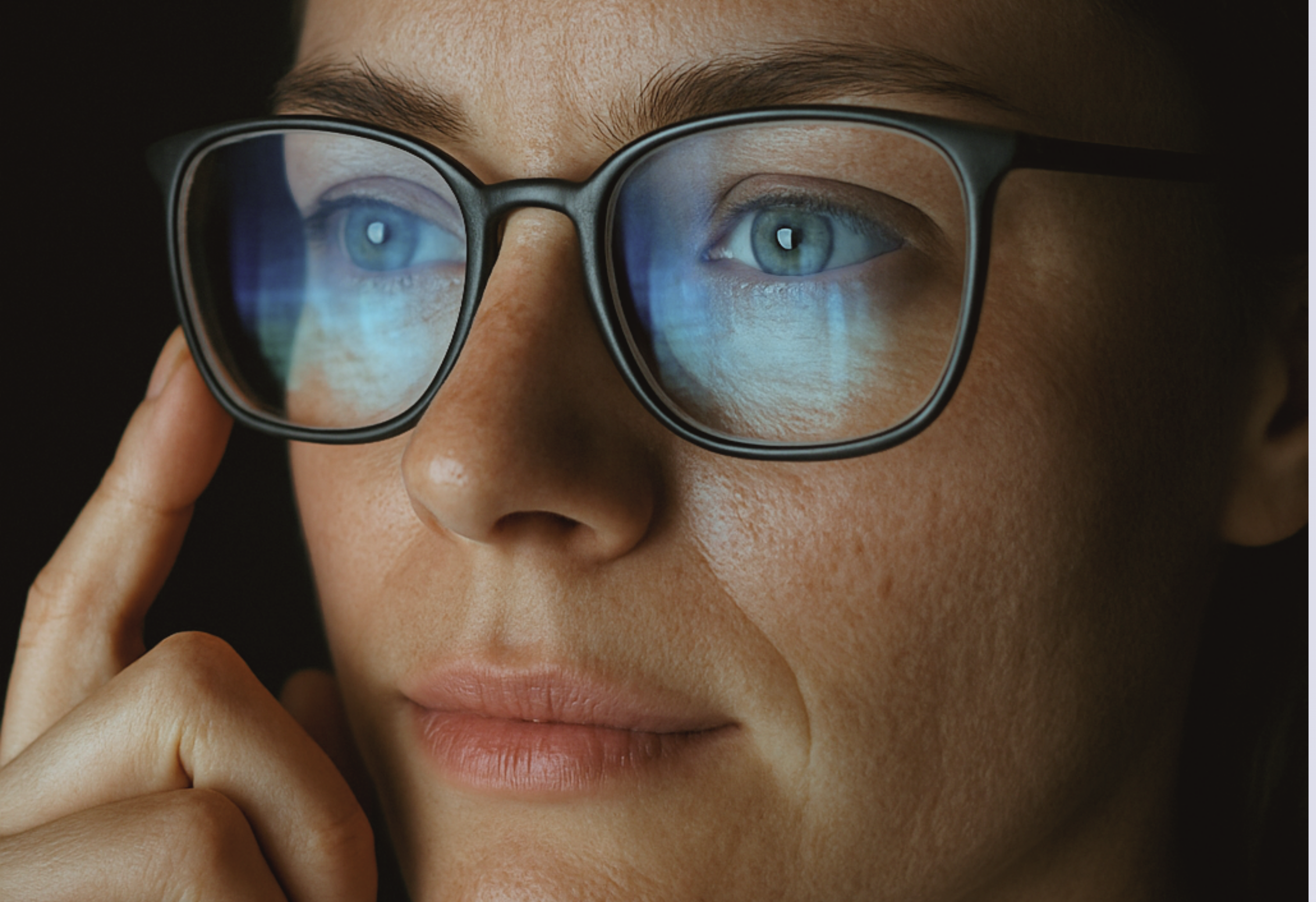 Nahaufnahme einer Frau mit Brille, in der sich das blaue Licht des Computers spiegelt