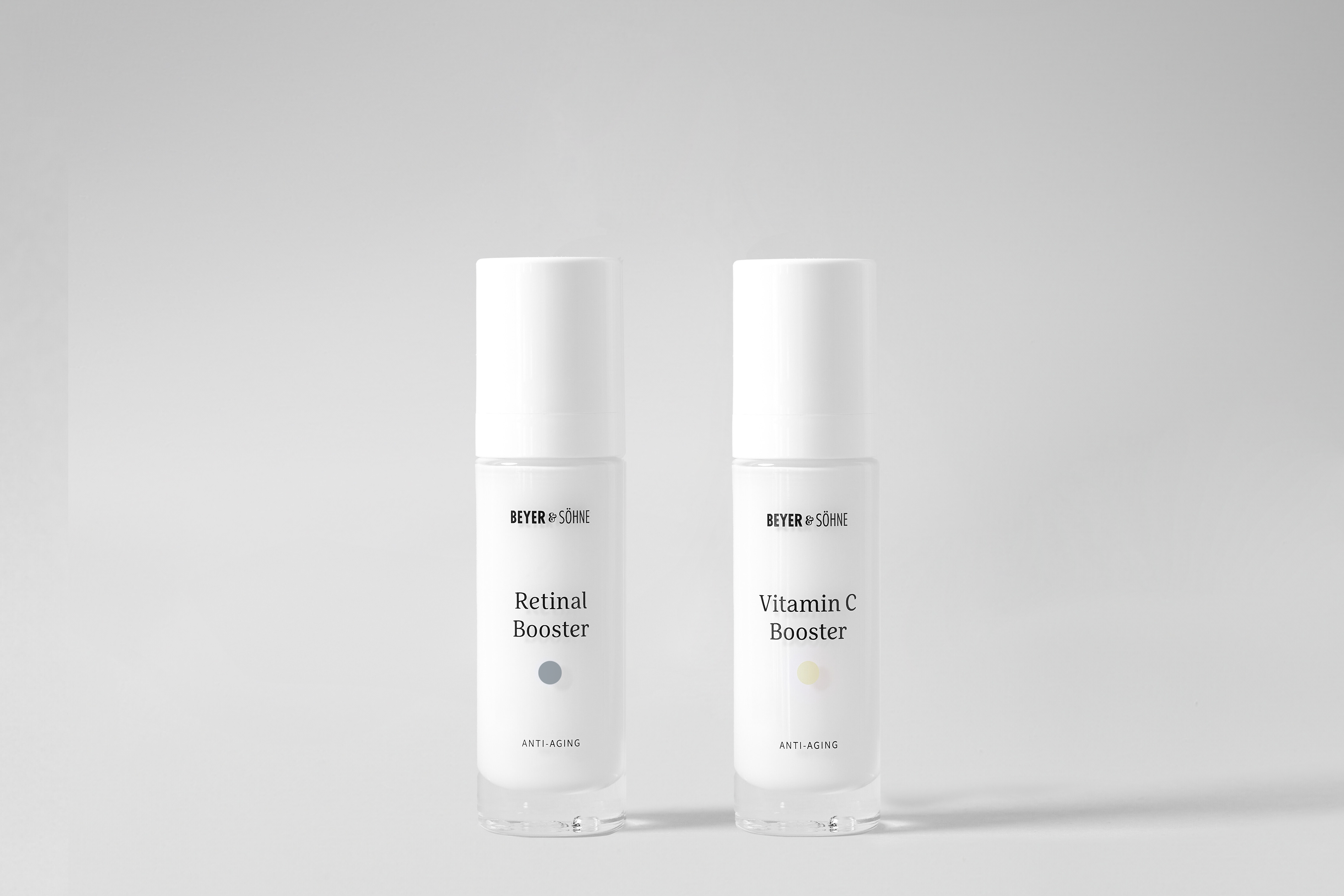 Zwei hochwertige Anti-Aging-Seren in licht- und luftdichter Verpackung. Links der Vitamin C Booster für strahlende Haut und Reduktion von Pigmentflecken, rechts der Retinal Booster zur Faltenminderung und Hauterneuerung. Minimalistisches Design, perfekt für empfindliche Haut.
