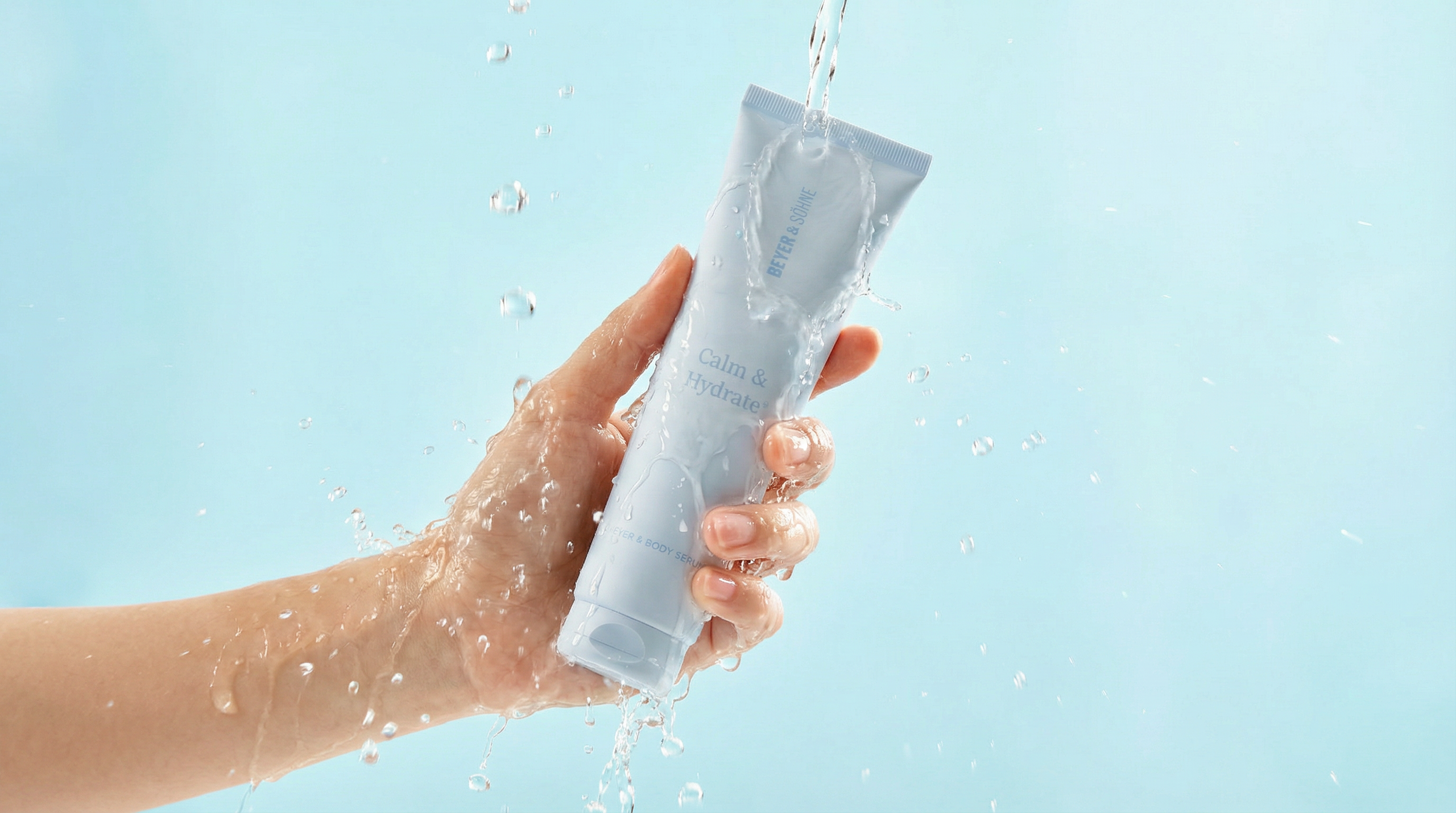 Eine Hand hält Calm & Hydrate+ unter fließendem Wasser. Die hellblaue Tube ist von Wasserperlen und Spritzern umgeben und vermittelt Frische, Feuchtigkeit und eine leichte Pflege.