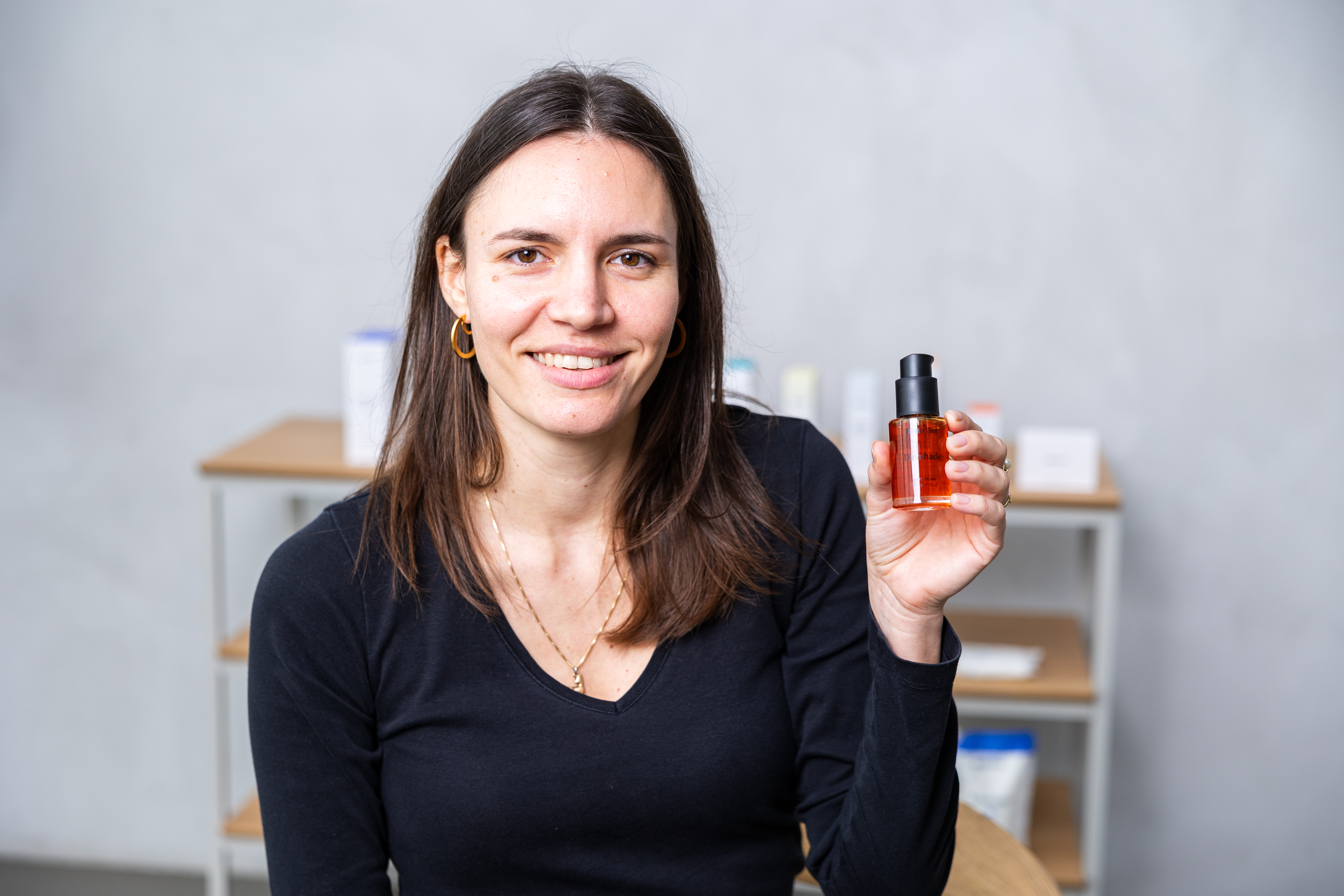 Junge natürliche Frau mit schulterlangem braunen Haar hält lächelnd Dayshade SPF 50+ in der Hand