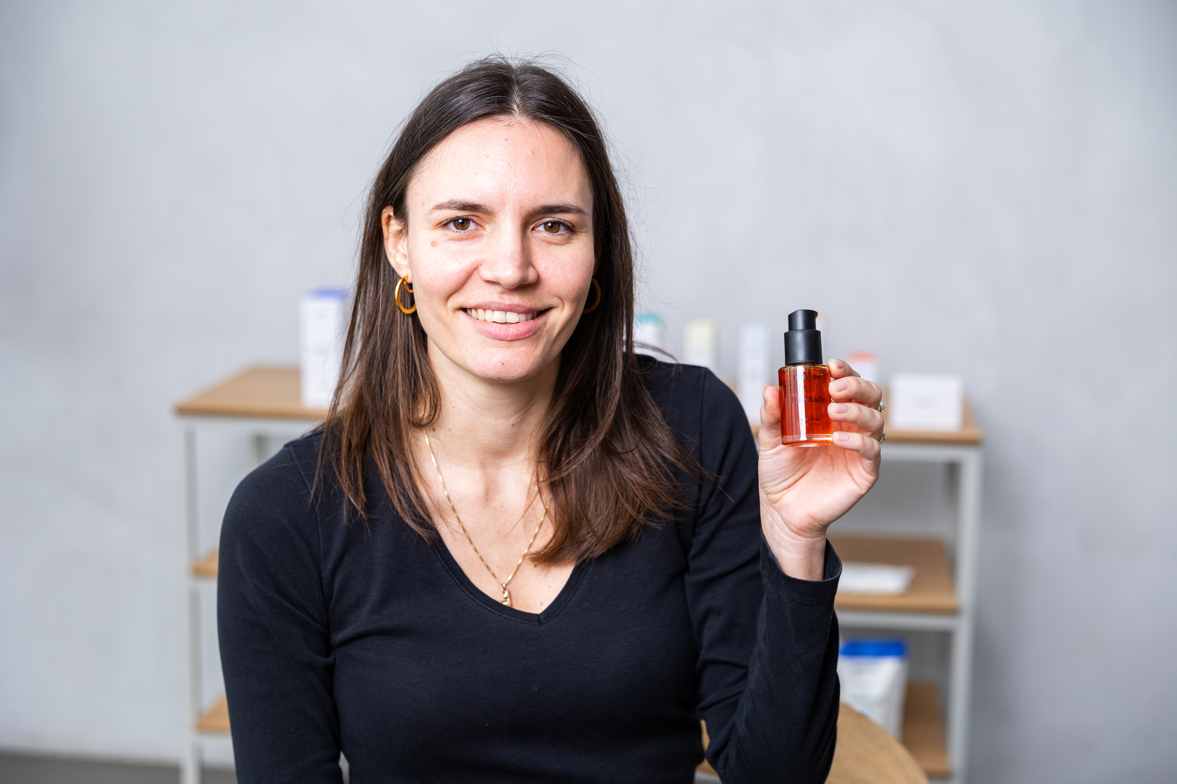Junge natürliche Frau mit schulterlangem braunen Haar hält lächelnd Dayshade SPF 50+ in der Hand