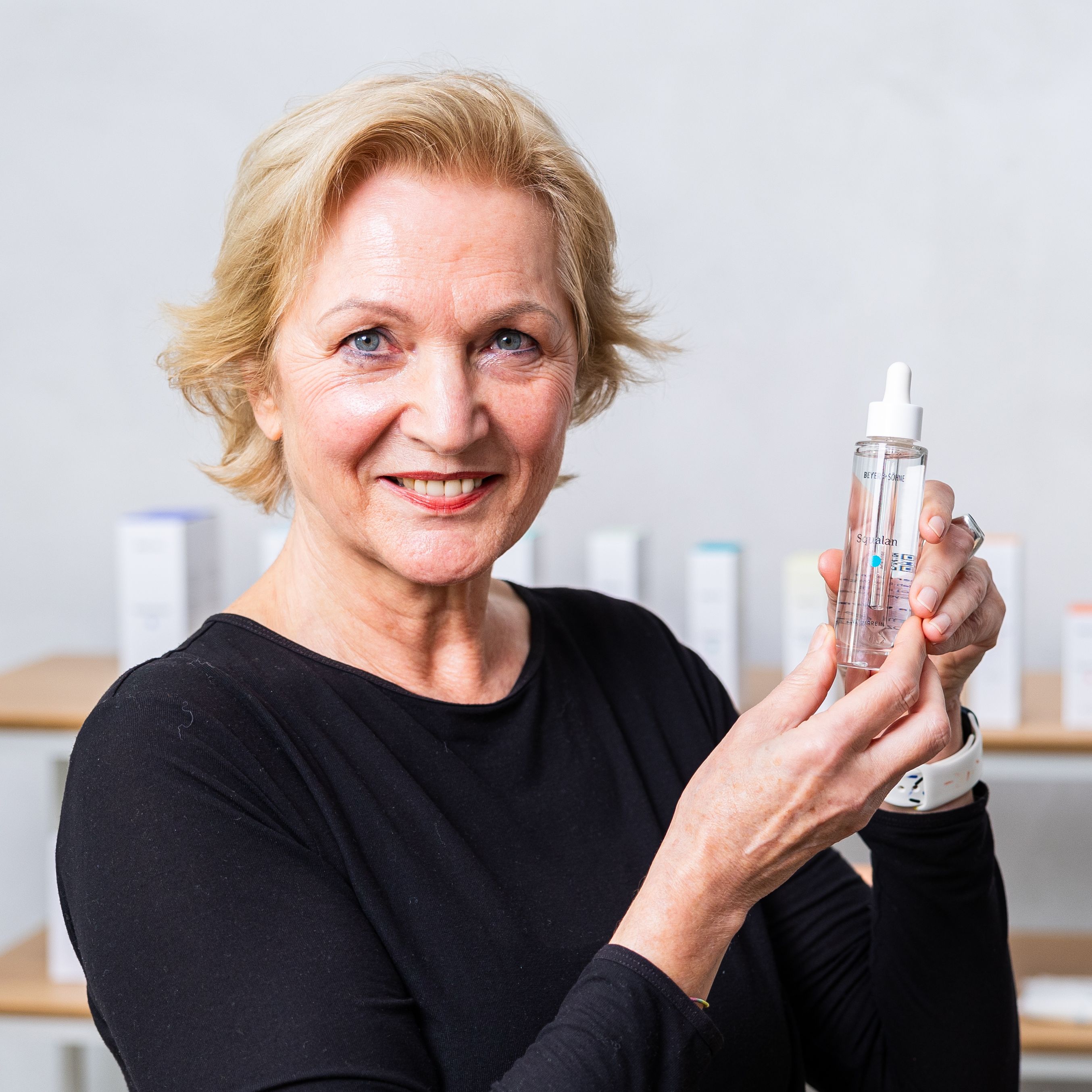 Natürliche Frau Ende 50 mit blondem, kurzen Haar lächelt in die Kamera und hält das Squalan von Beyer & Söhne in den Händen