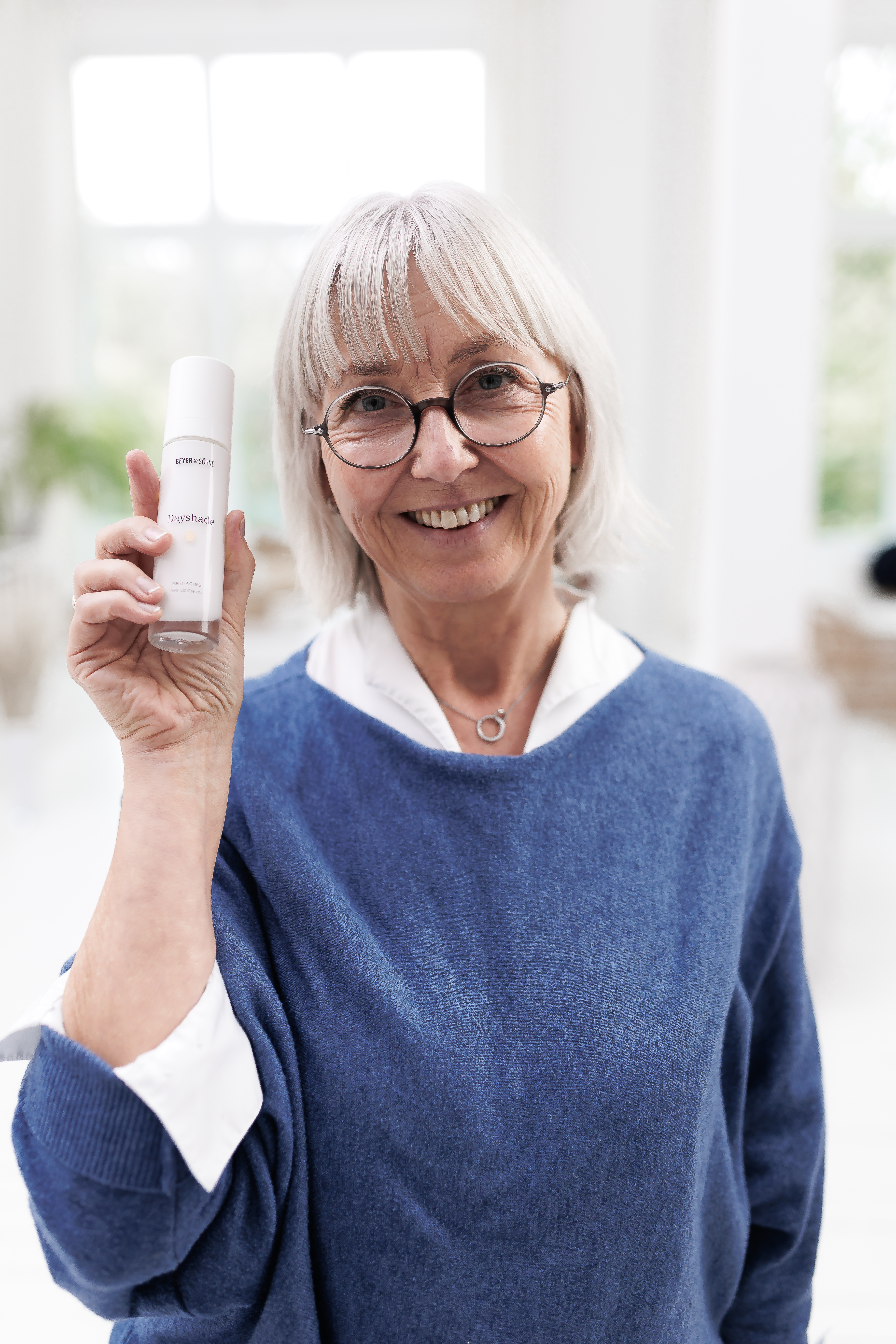 Lächelnde Frau mit Brille und einer Dayshade Cream in der Hand
