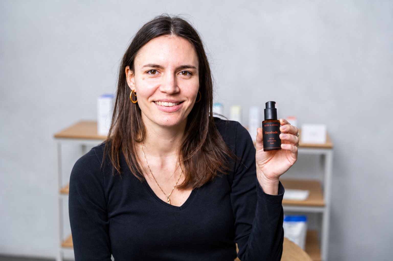 Junge natürliche Frau mit schulterlangem braunen Haar hält lächelnd Dayshade SPF 50 in der Hand