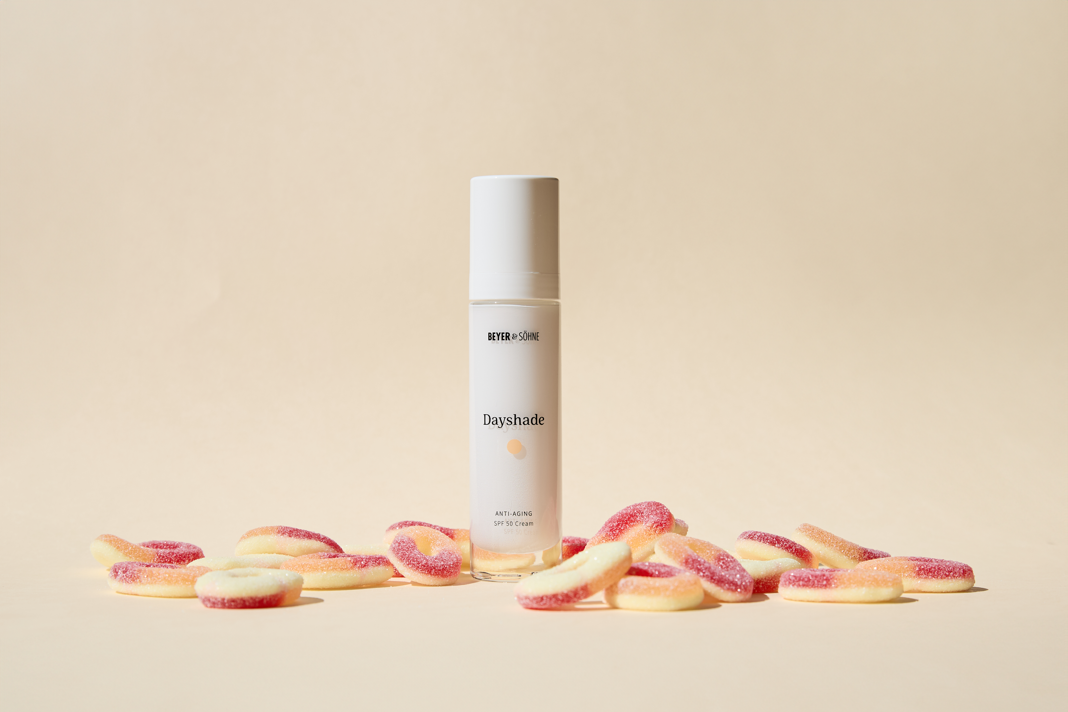 Dayshade Cream von Beyer & Söhne mit LSF 50 zwischen sauren Pfirsichringe vor schlichter beiger Wand