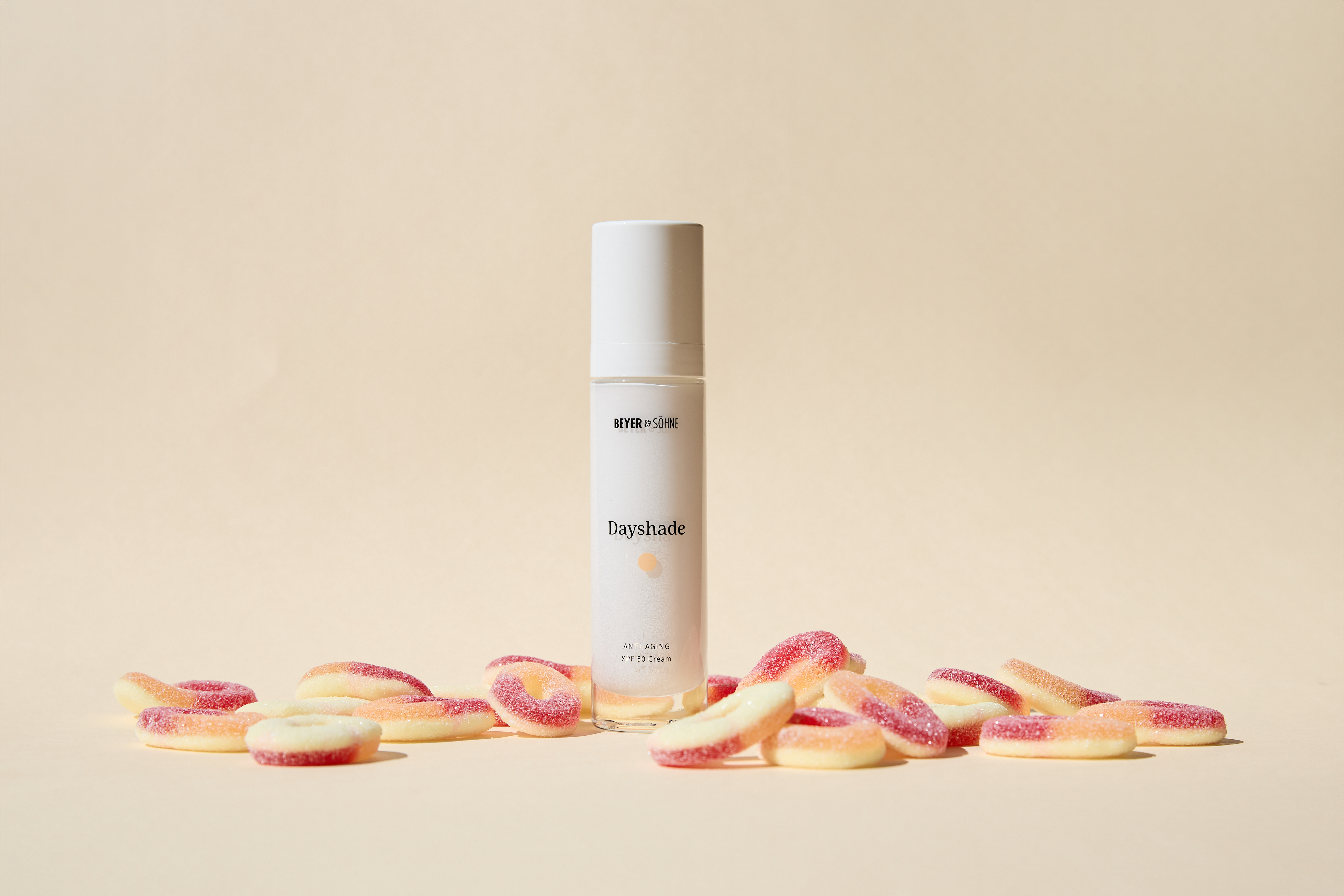 Dayshade Cream von Beyer & Söhne mit LSF 50 zwischen sauren Pfirsichringe vor schlichter beiger Wand