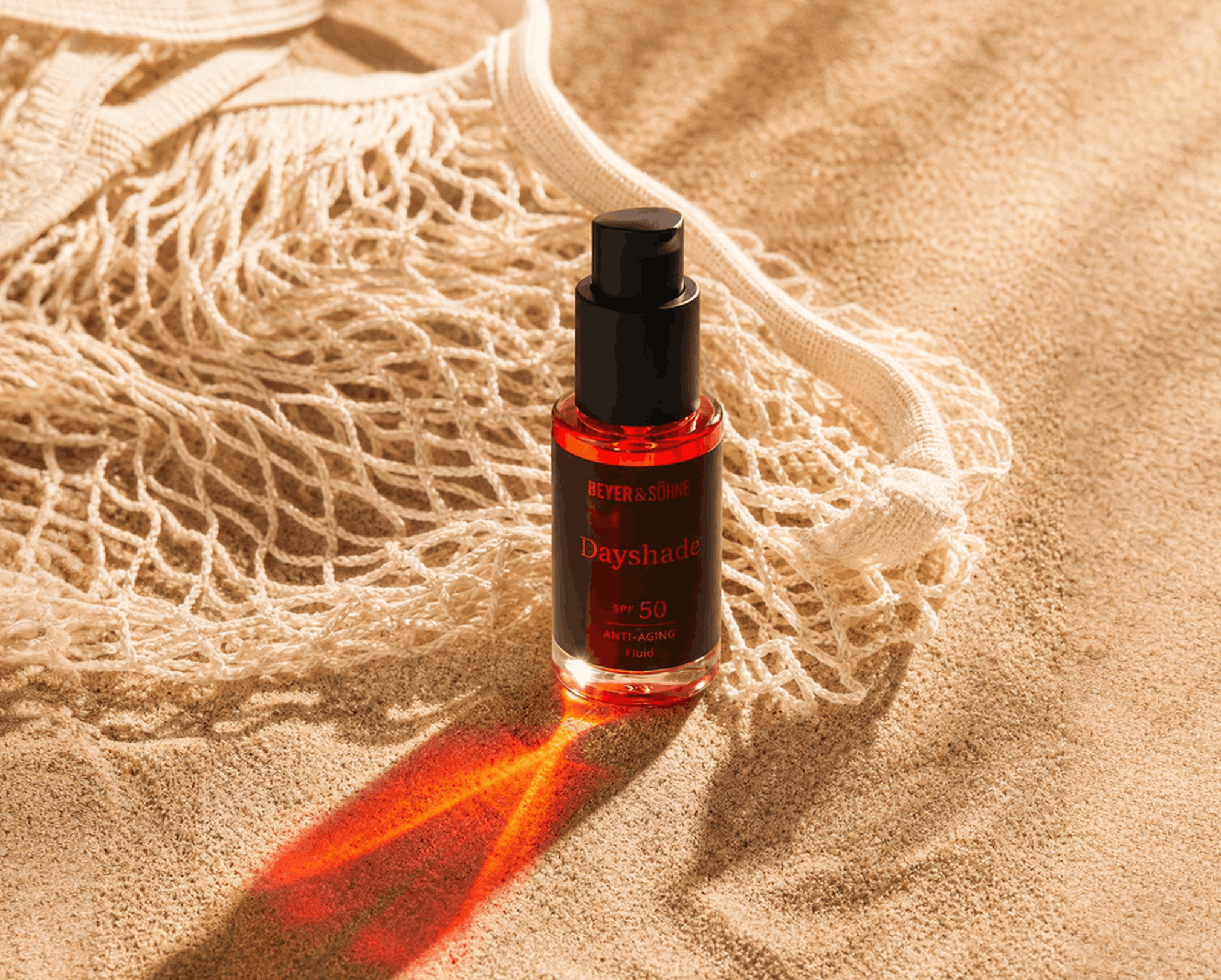 Beyer & Söhne Dayshade Fluid LSF 50 auf Sand mit Netztasche und rotem Lichtreflex in der Sonne