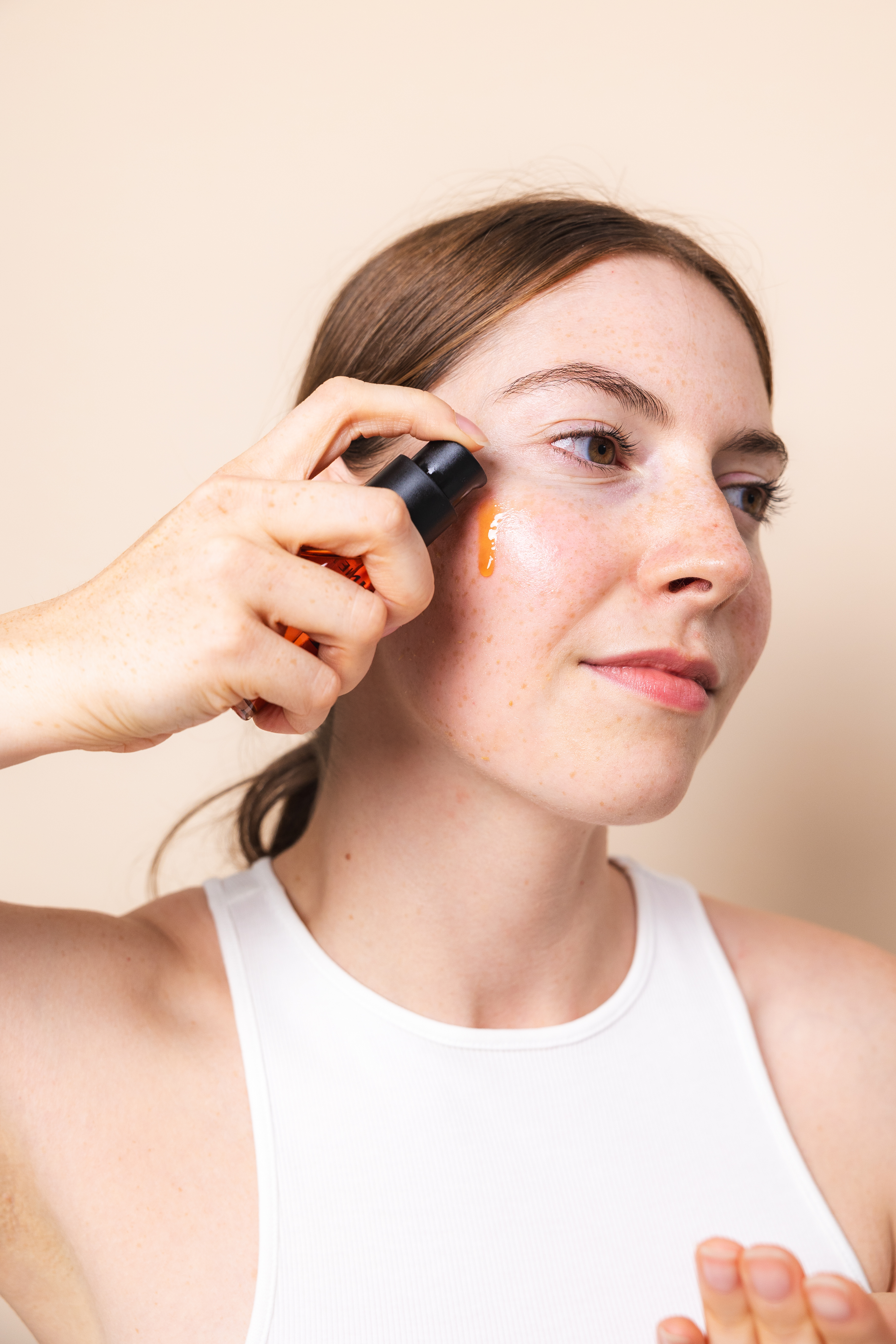 Eine Person trägt das Dayshade Fluid LSF 50 direkt aus dem Spender auf die Wange auf. Sie hält den Spender in der Hand, während ein Tropfen des leichten, orangefarbenen Fluids auf der Haut sichtbar ist. Die Aufnahme zeigt die einfache Anwendung und die flüssige Textur des Sonnenschutzes.