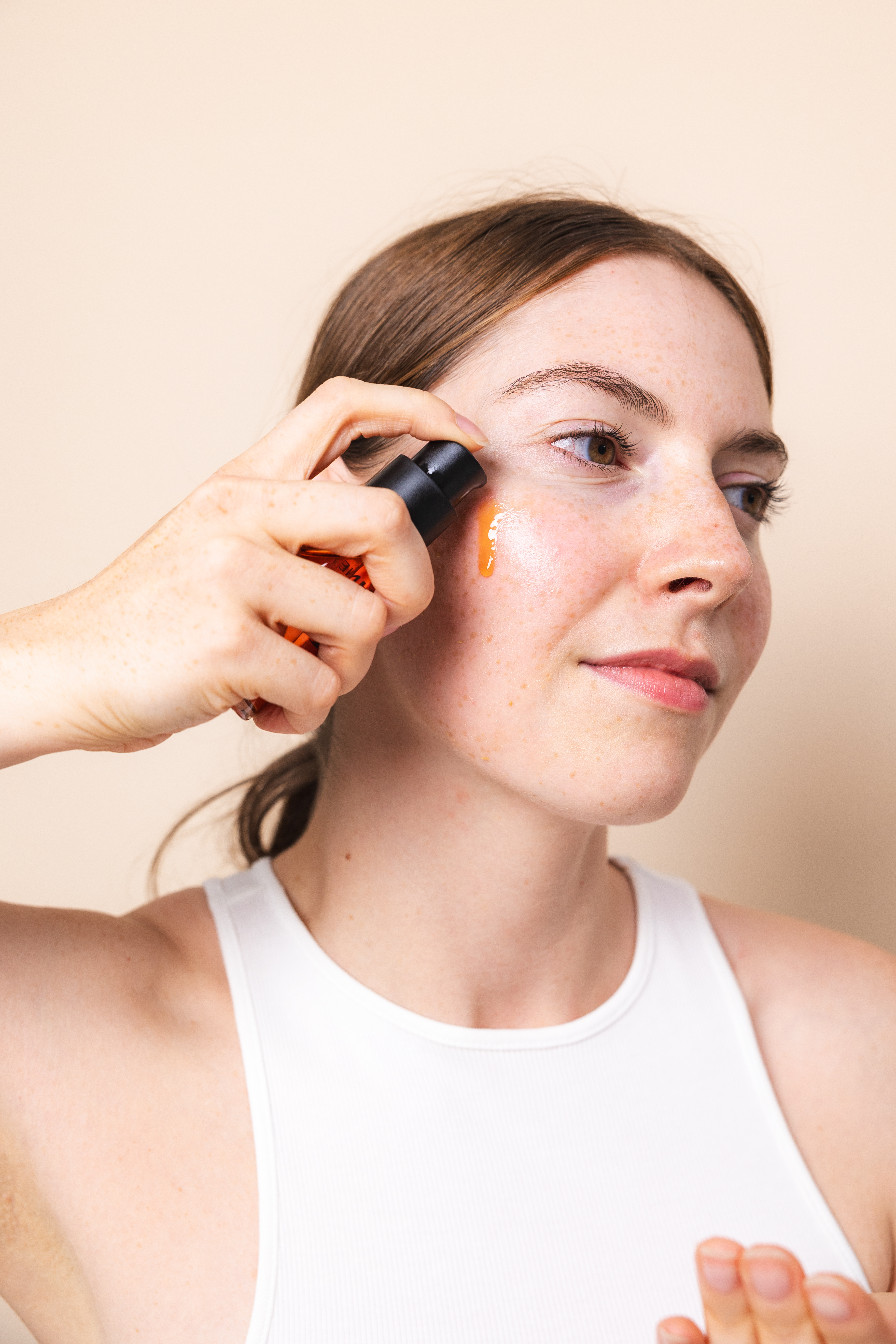 Eine Person trägt das Dayshade Fluid LSF 50 direkt aus dem Spender auf die Wange auf. Sie hält den Spender in der Hand, während ein Tropfen des leichten, orangefarbenen Fluids auf der Haut sichtbar ist. Die Aufnahme zeigt die einfache Anwendung und die flüssige Textur des Sonnenschutzes.