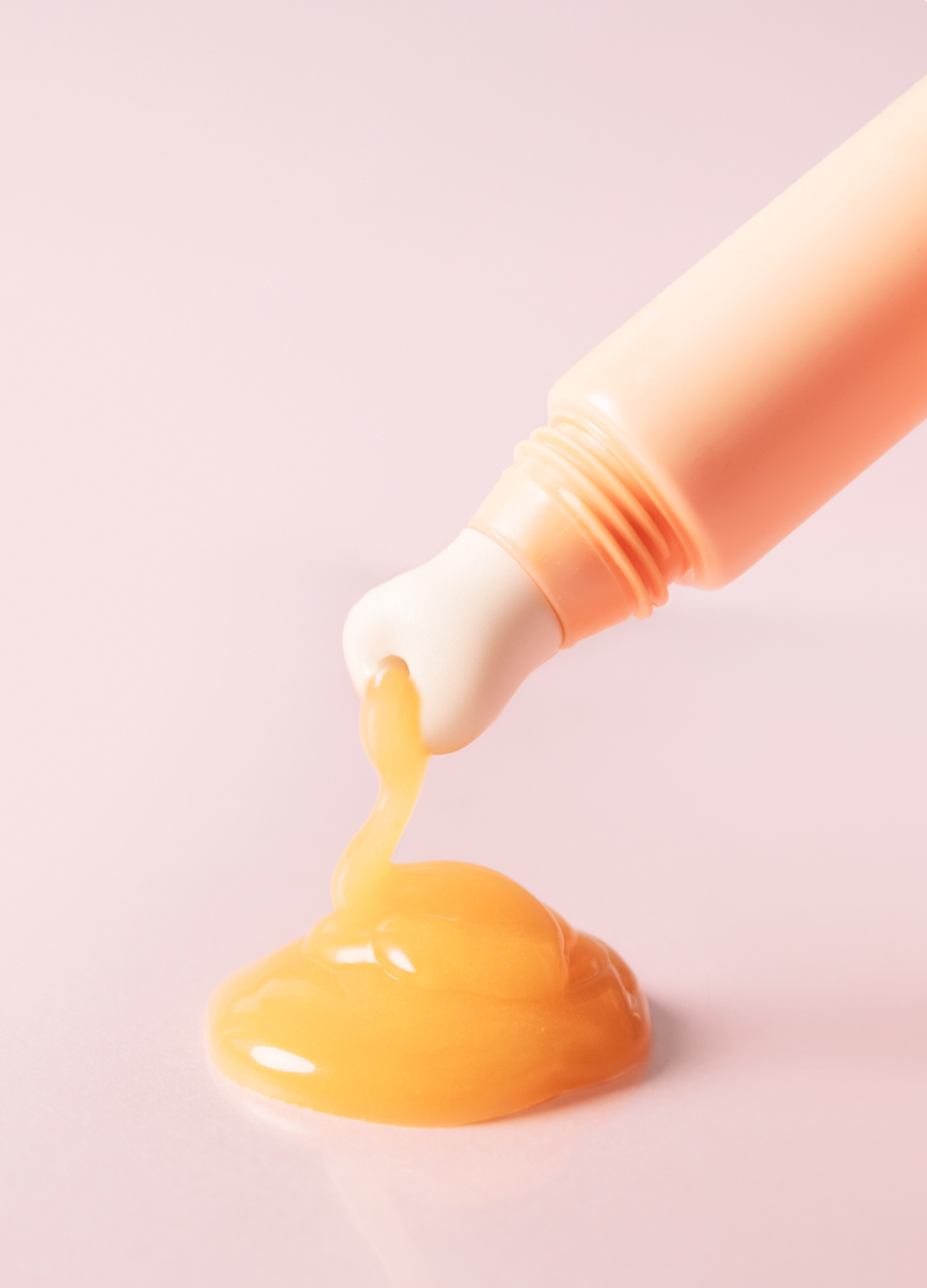 Dayshade Lip Balm SPF 50+ mit Keramik Applikatorspitze, aus der ein Tropfen goldener Balsam fließt, auf zartem rosa Hintergrund.