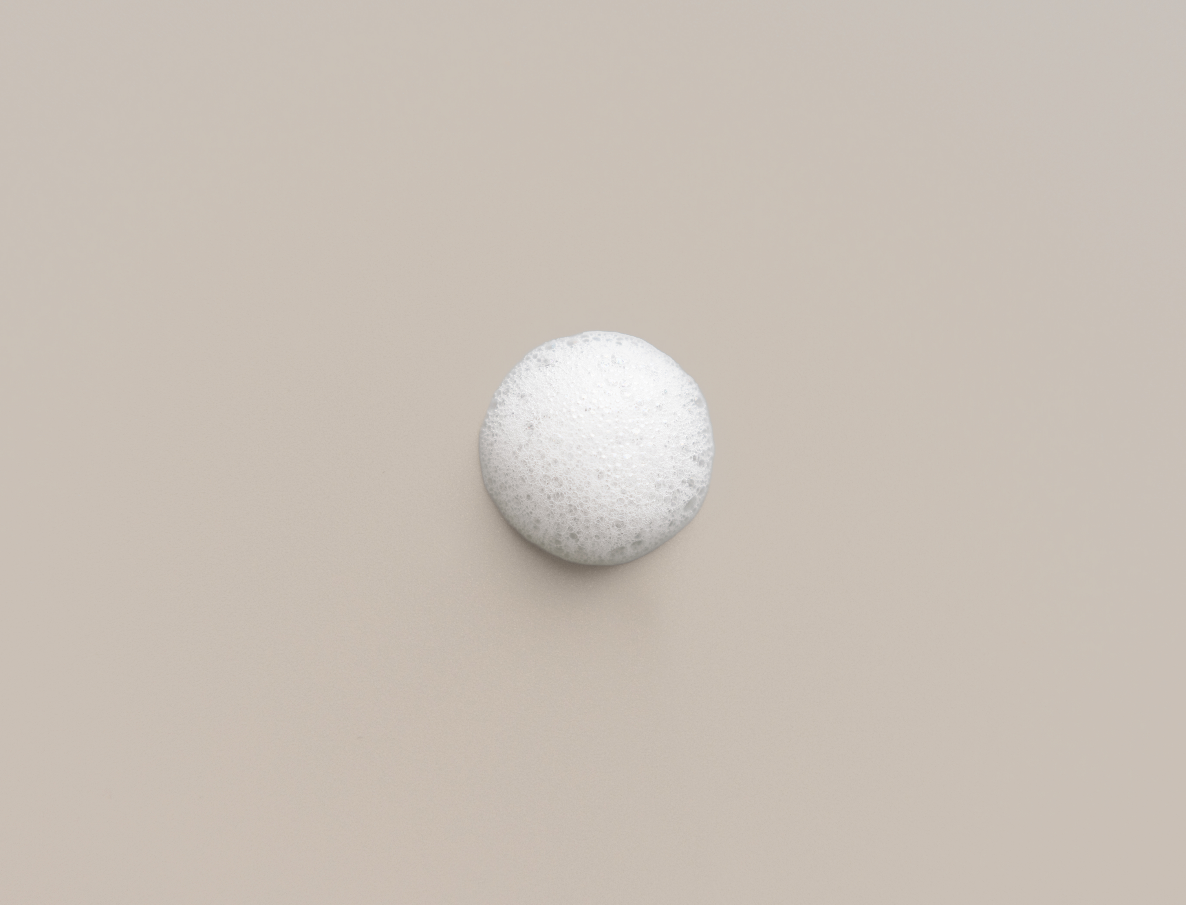Schaumtropfen mit feinen, gleichmäßigen Bläschen auf neutralem, beigen Untergrund. Darstellung der leichten, cremigen Konsistenz des Foam Cleansers von Beyer & Söhne