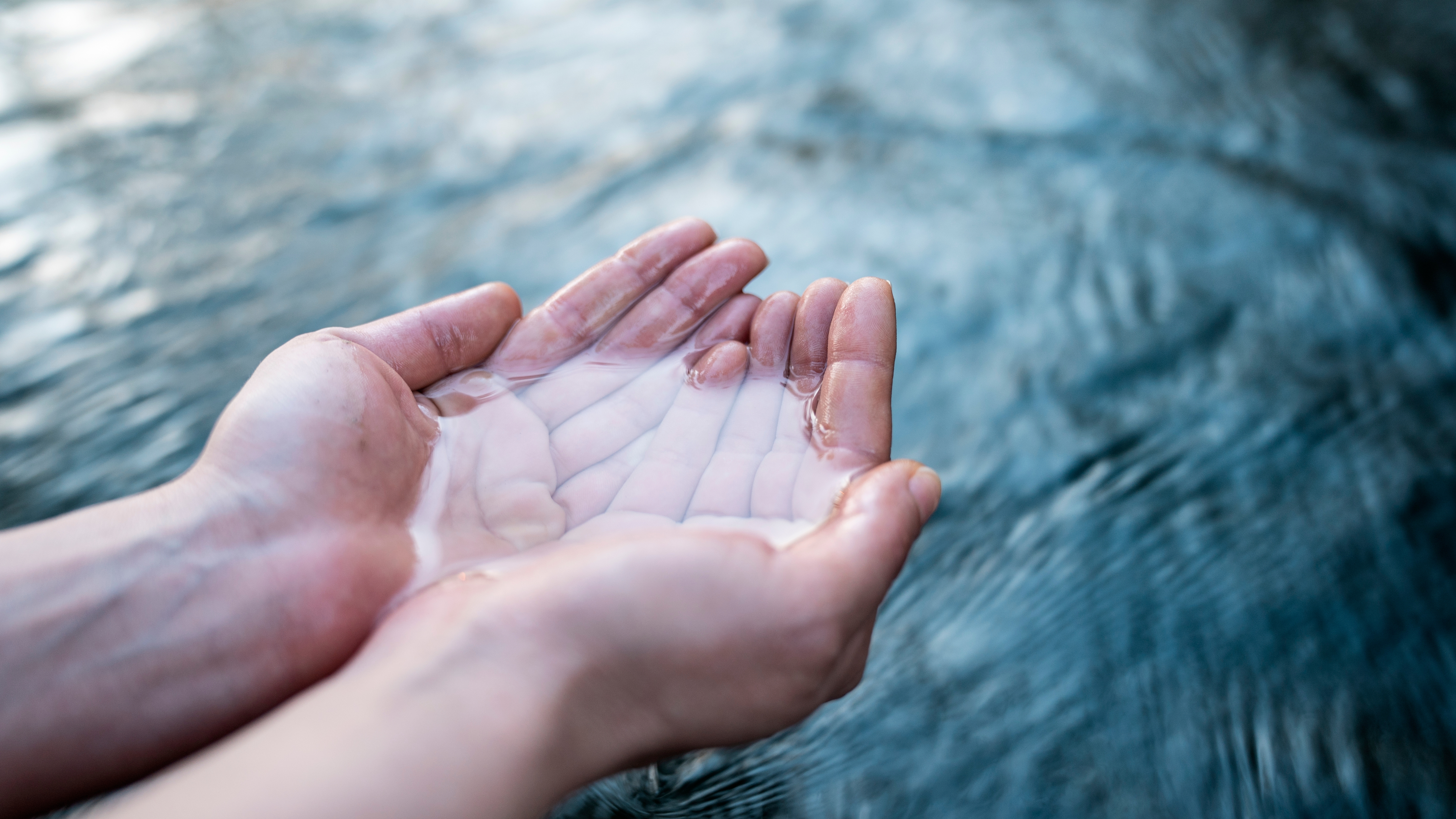 Zwei HĂ€nde, die klares Flusswasser berĂŒhren