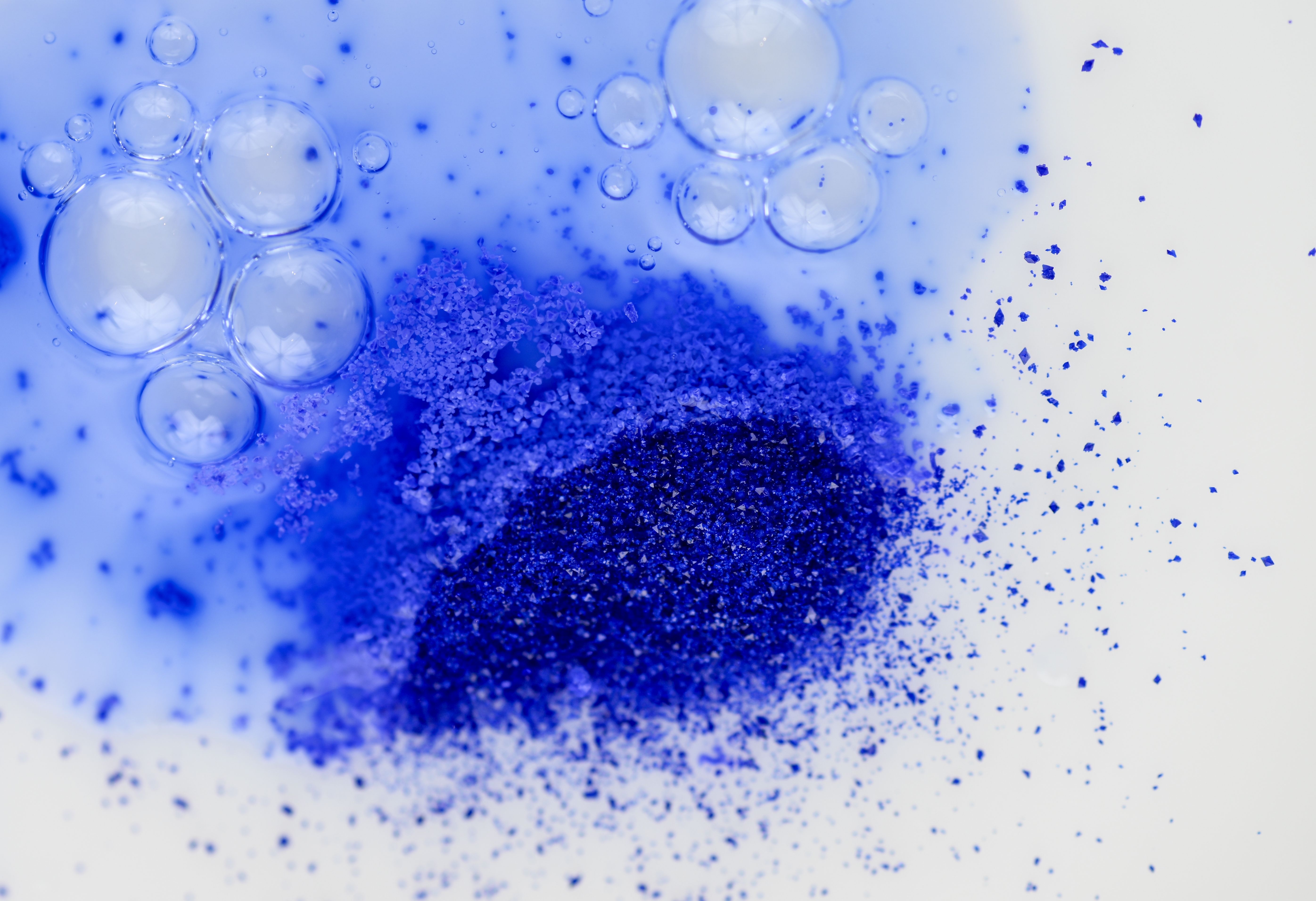 Blaue Kupferpeptide in Pulverform vermischen sich in einem transparenten Serum auf hellem Hintergrund.