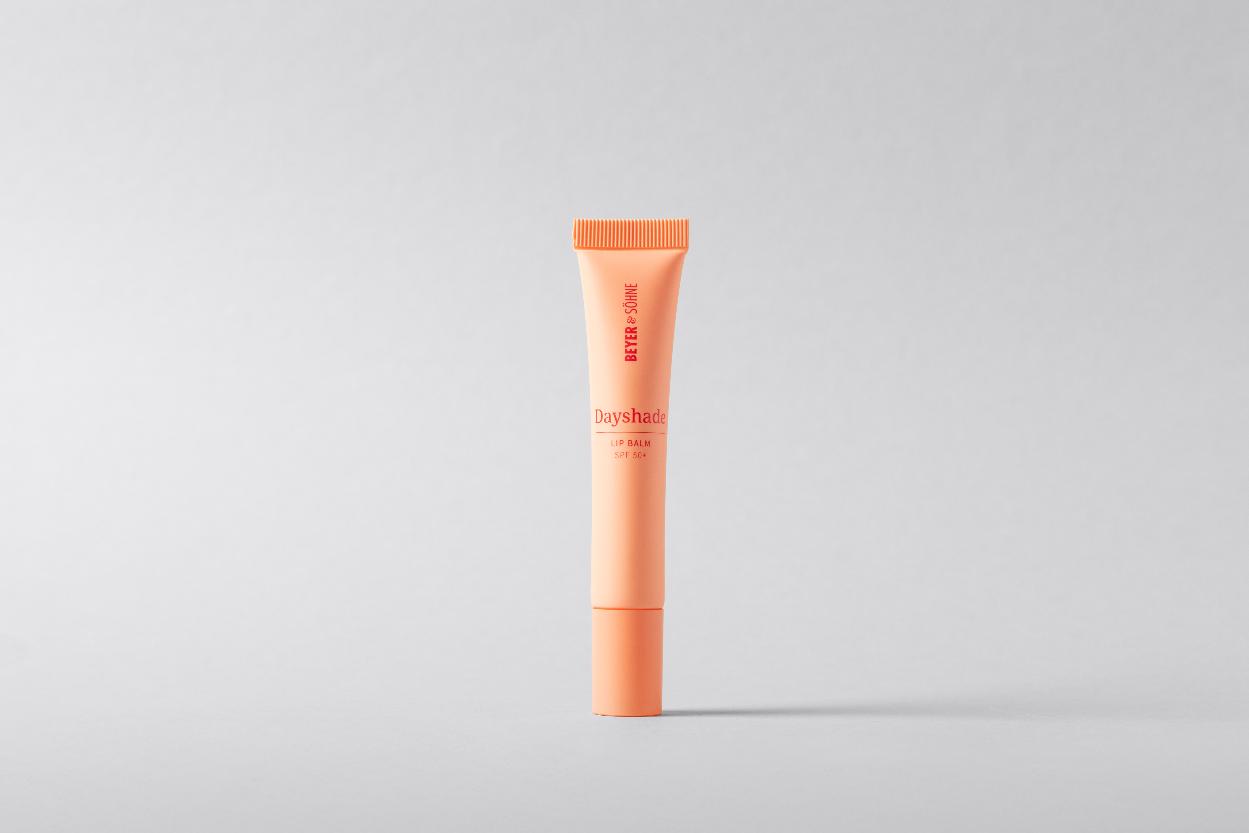 Beyer & Söhne Dayshade Lip Balm SPF 50+ in einer minimalistischen, pfirsichfarbenen Tube vor neutralem Hintergrund, eleganter und stark pflegender Sonnenschutz für die Lippen