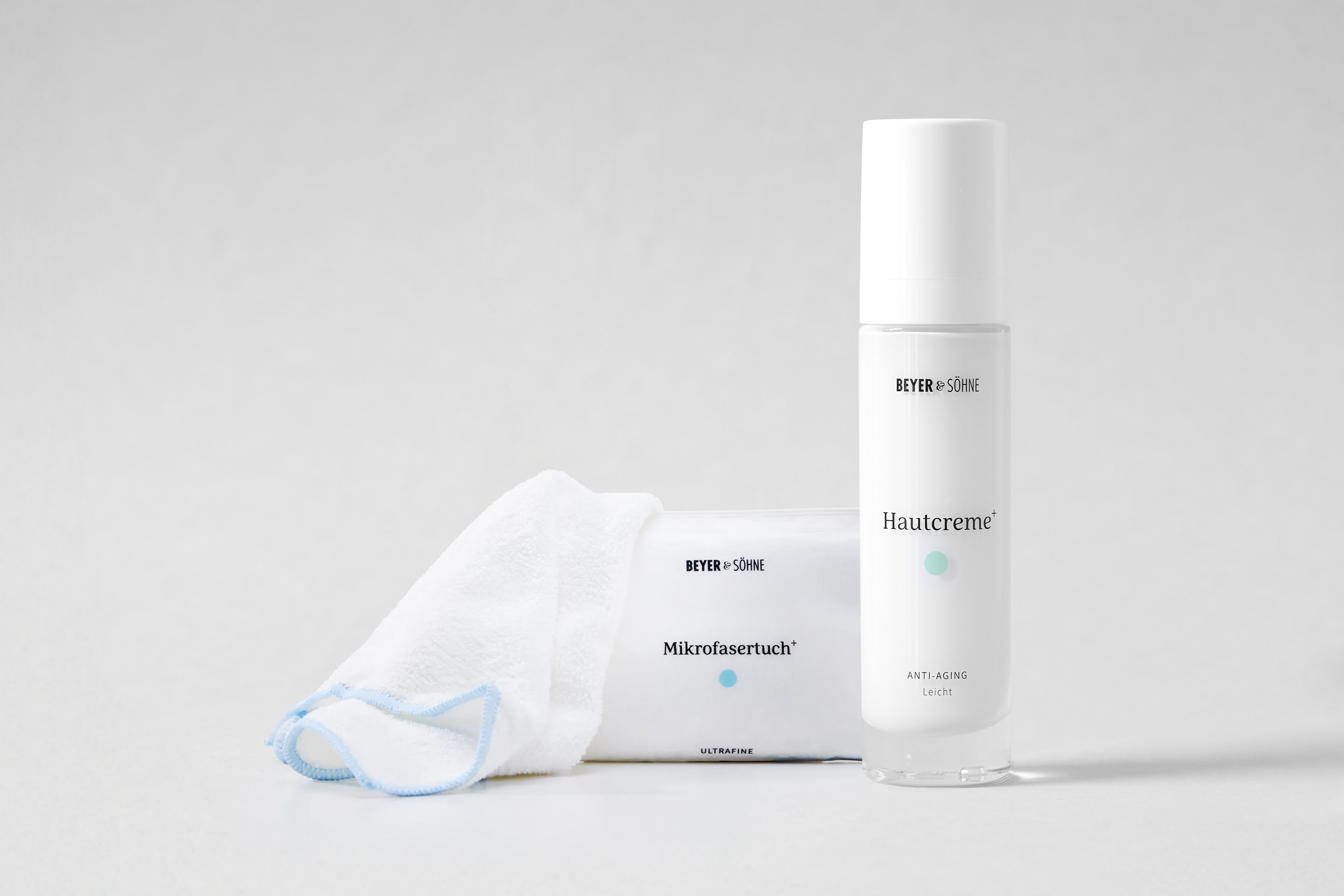 Hautcreme+ Anti-Aging Leicht und Mikrofasertuch+ vor neutral hellem Hintergrund. Die reduzierte Inszenierung betont die hochwertige Pflegeroutine und das minimalistische Produktdesign.