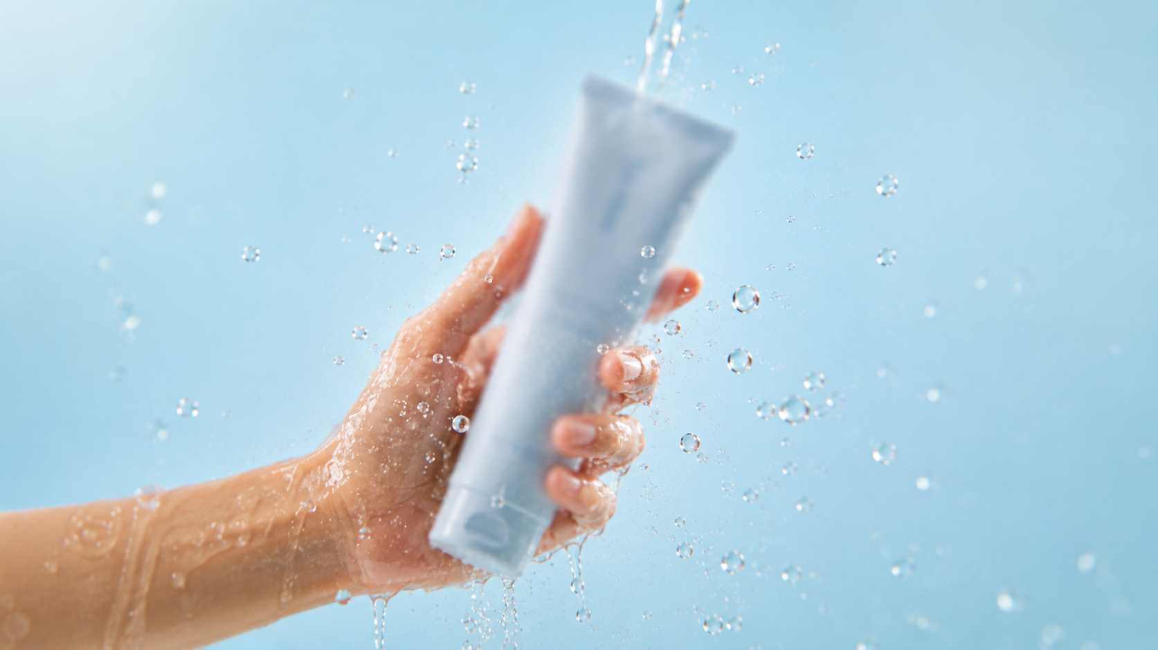 Ein neues Produkt von Beyer & Söhne, das bald eingeführt wird. Eine Hand hält die himmelblaue und mit Absicht verschwommene Tube in der Hand, während Wasser niederprasselt. Das Bild vermittelt Feuchtigkeit.