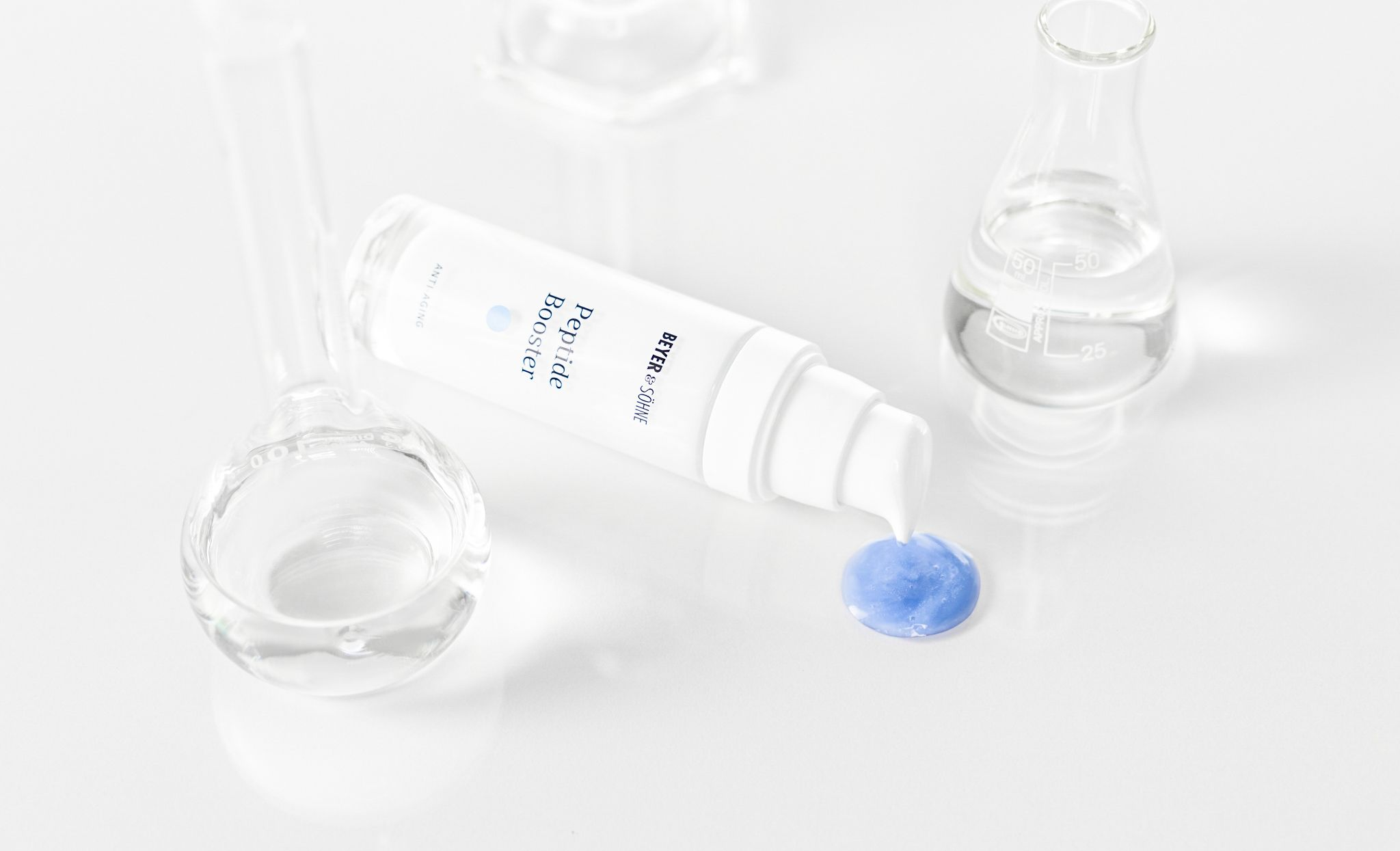 Peptide Booster von Beyer & Söhne in weißer, minimalistisch eleganten Flasche mit blauer Serumtextur, inszeniert zwischen gläsernen Laborgefäßen auf hellem Hintergrund.