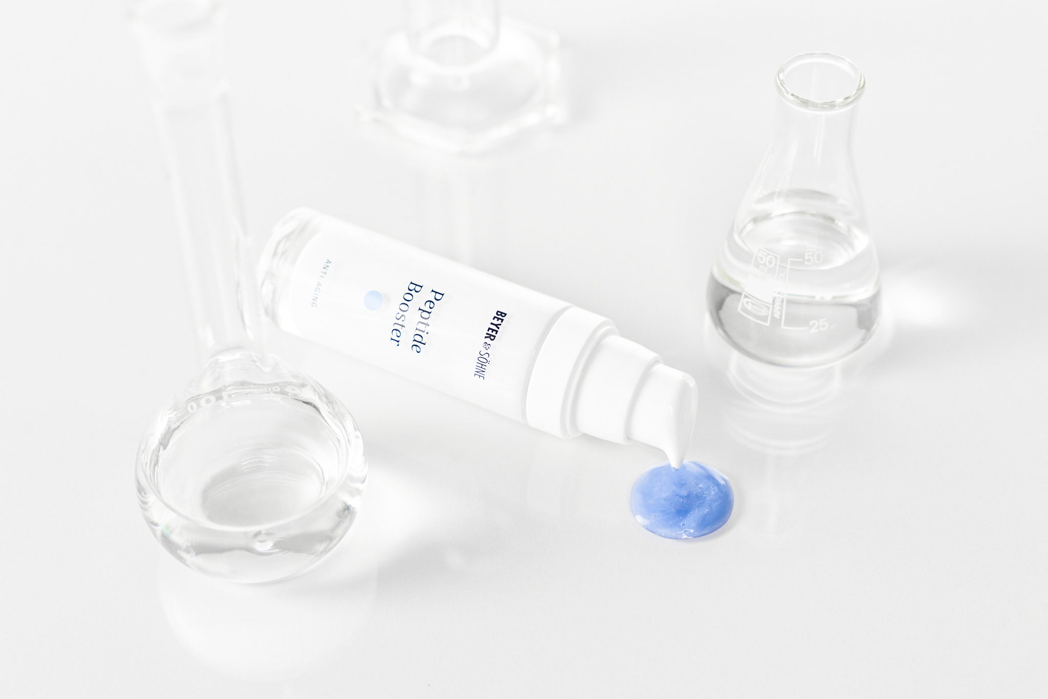 Peptide Booster von Beyer & Söhne in weißer, minimalistisch eleganten Flasche mit blauer Serumtextur, inszeniert zwischen gläsernen Laborgefäßen auf hellem Hintergrund.