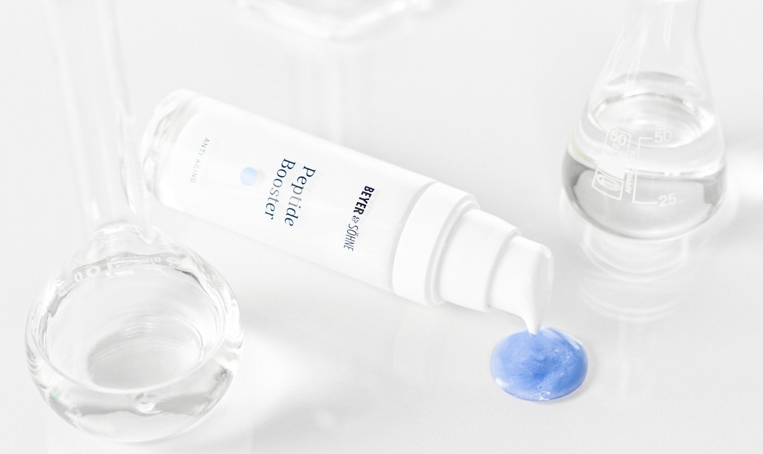 Peptide Booster von Beyer & Söhne in weißer, minimalistisch eleganten Flasche mit blauer Serumtextur, inszeniert zwischen gläsernen Laborgefäßen auf hellem Hintergrund.