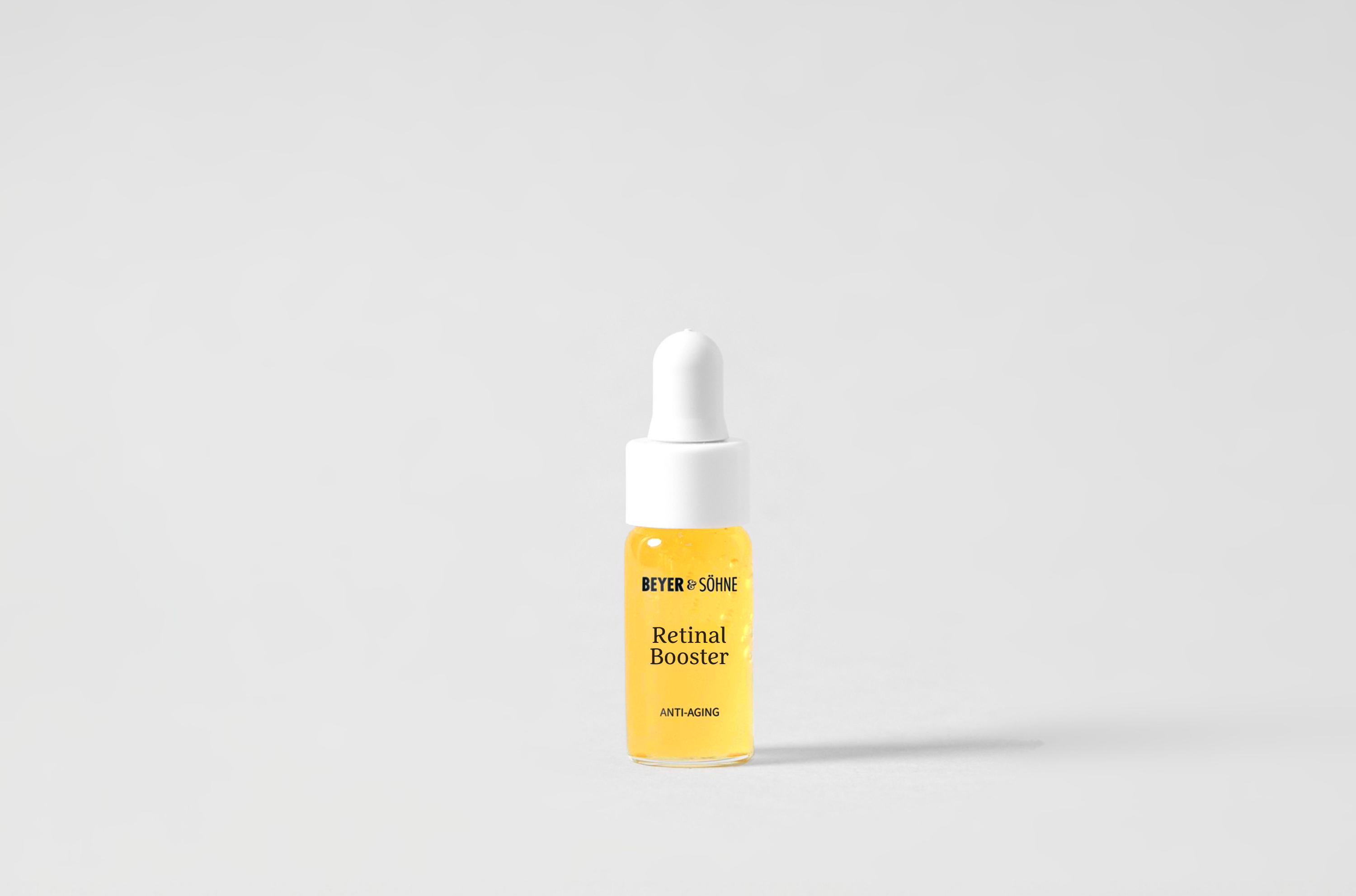 Goldgelber Retinal Booster von Beyer & Söhne in niedlicher Tester-Größer aus Glas mit kleiner Pipette vor schlichten grauen Hintergrund.