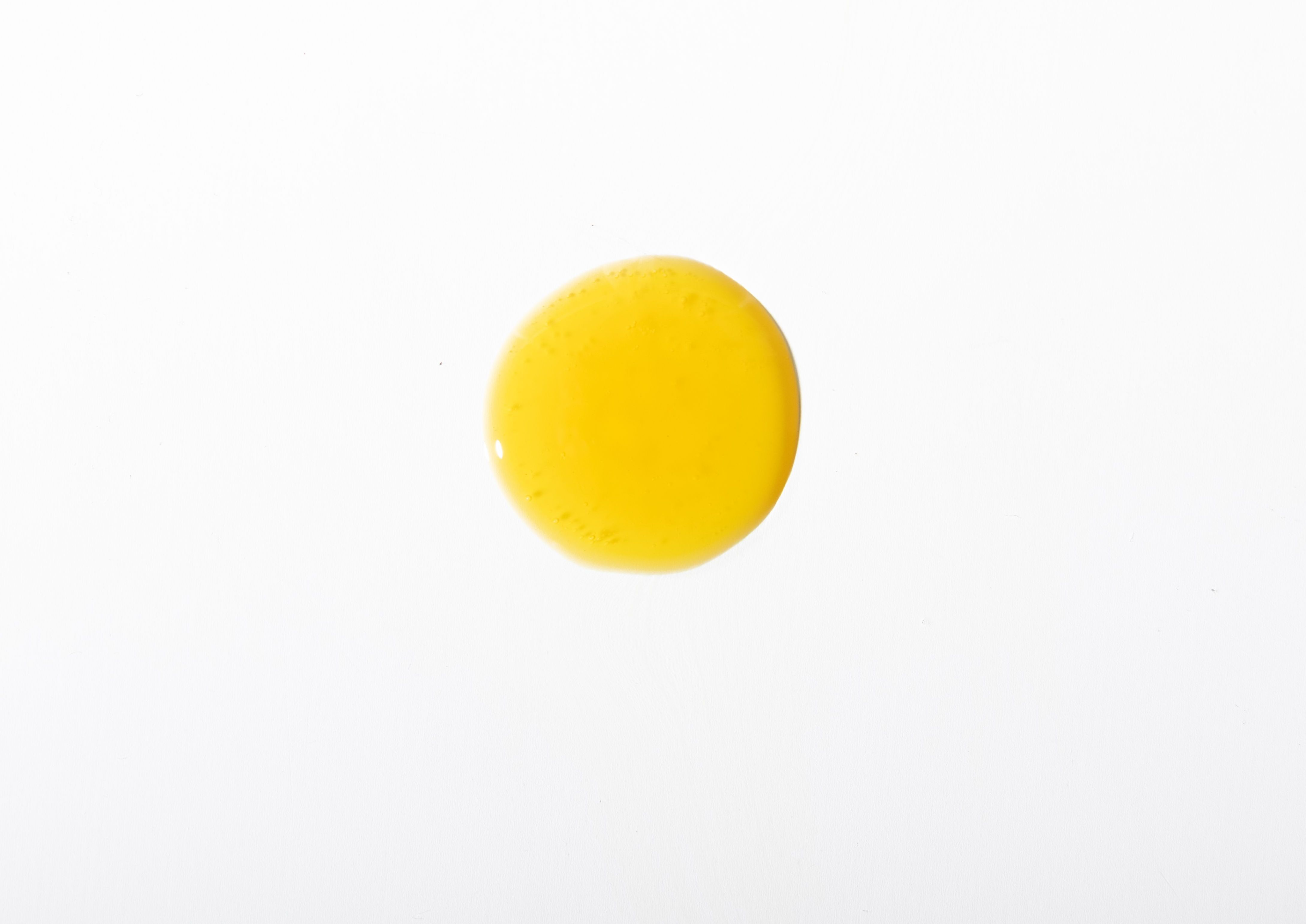 Eine gelbgoldene Fluid Textur als runder tropfen auf neutralem, hellgrauen Hintergrund stellt den Retinal Booster dar.