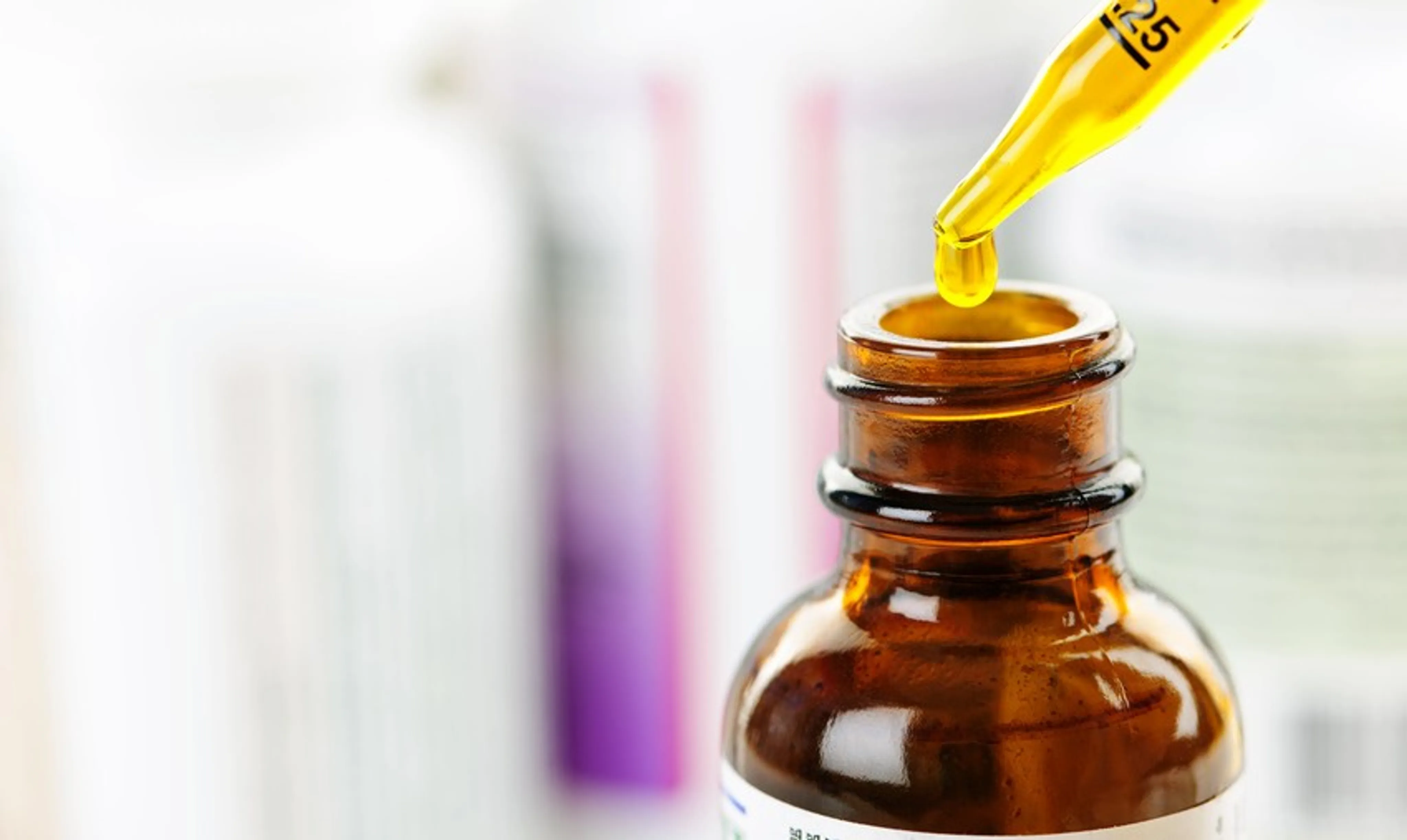 Nahaufnahme einer Pipettenspitze mit gelber Flüssigkeit, die Retinol darstellt, und über einer offenen braunen Medizinflasche gehalten wird.