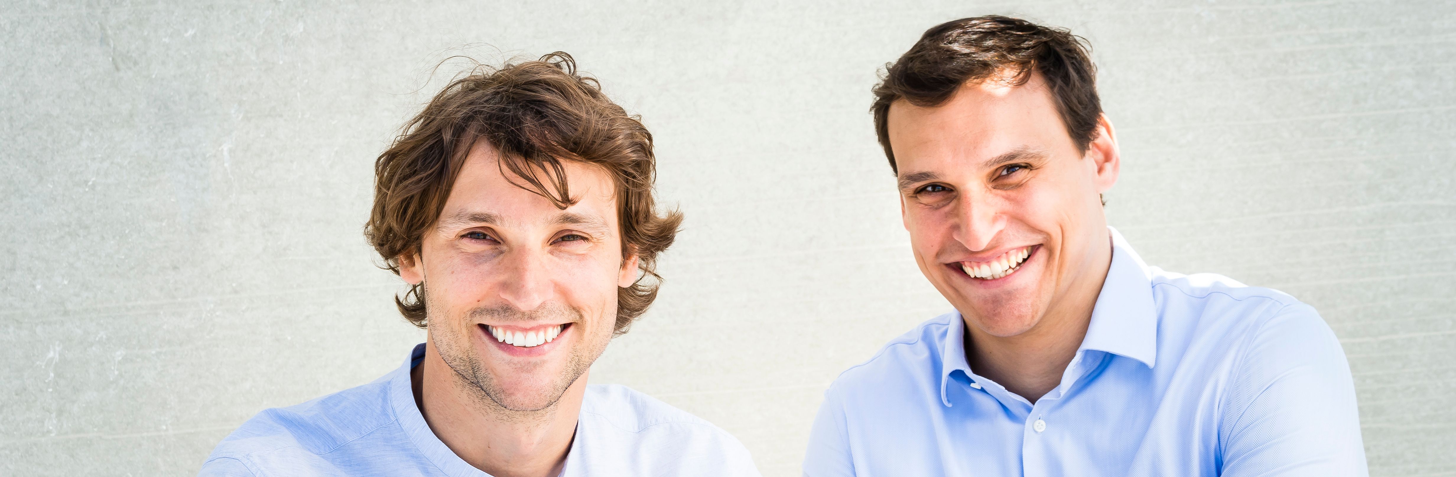 Zwei Männer mit dunklem Haar in hellblauen Hemden mit herzlichem Lachen, offen und sympathisch – Gründer von Beyer & Söhne, Robby und Nico Beyer.