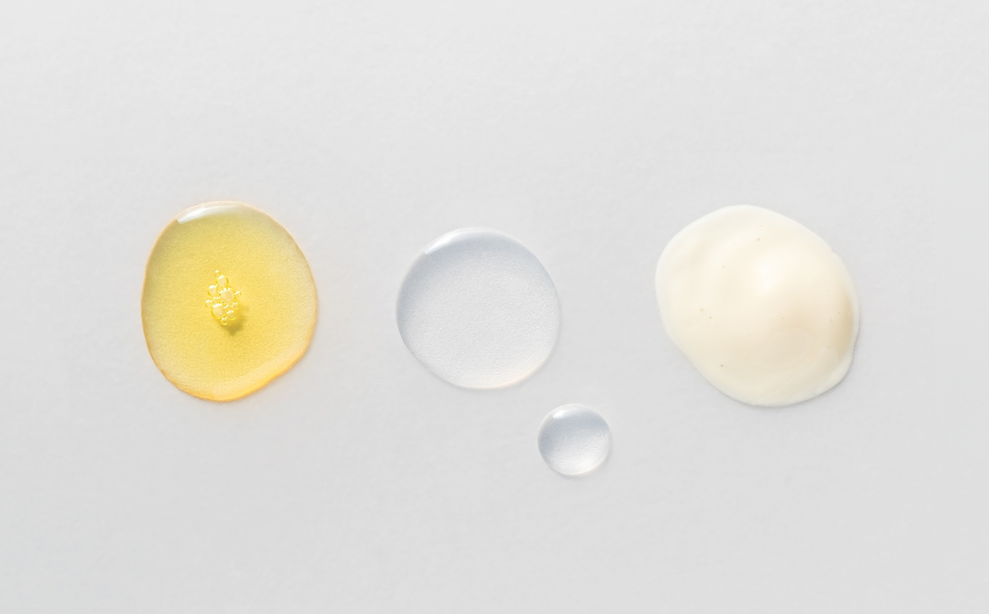 Drei unterschiedliche Texturen von Hautpflegeprodukten auf grauem Hintergrund: eine goldgelbe, eine klare und eine cremige weiße Textur. Darstellung der Vielfalt und hochwertigen Formulierungen der Produkte von Beyer & Söhne