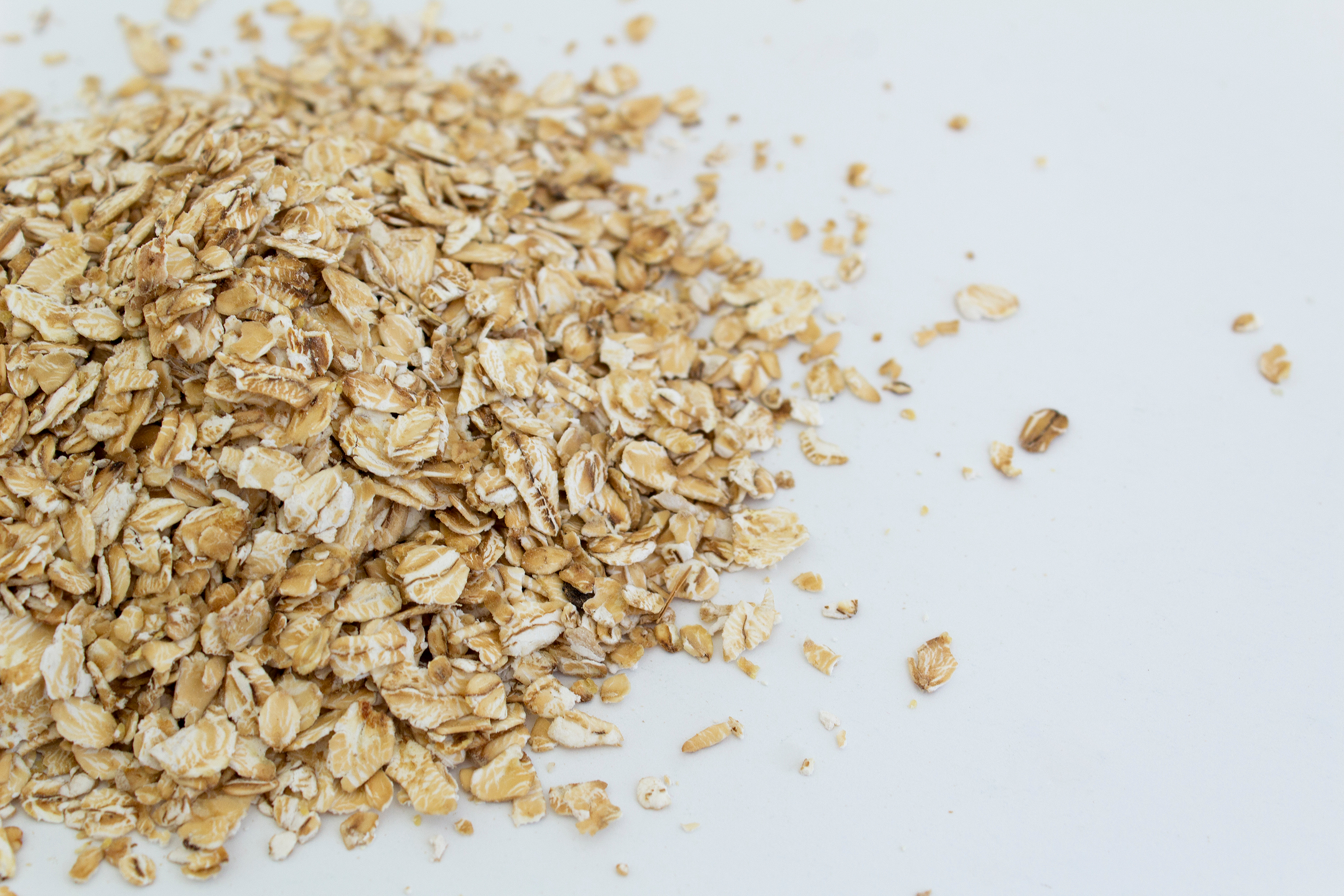 Haferflockenhaufen auf weißem Hintergrund symbolisieren Hafer-Aminosäuren als pflegenden Inhaltsstoff